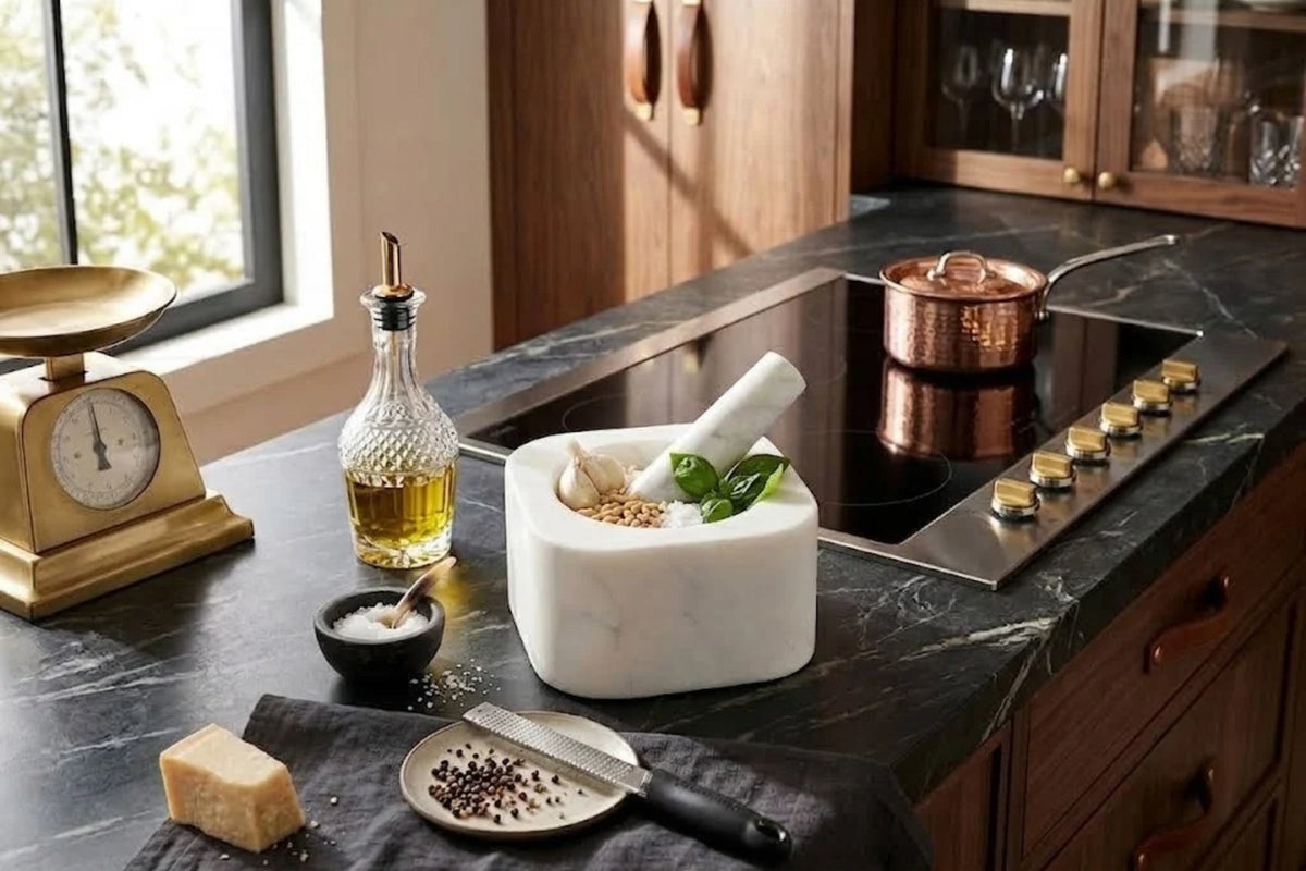 White marble mortar and pestle holding garlic, pine nuts, salt and basil on a dark stone kitchen counter