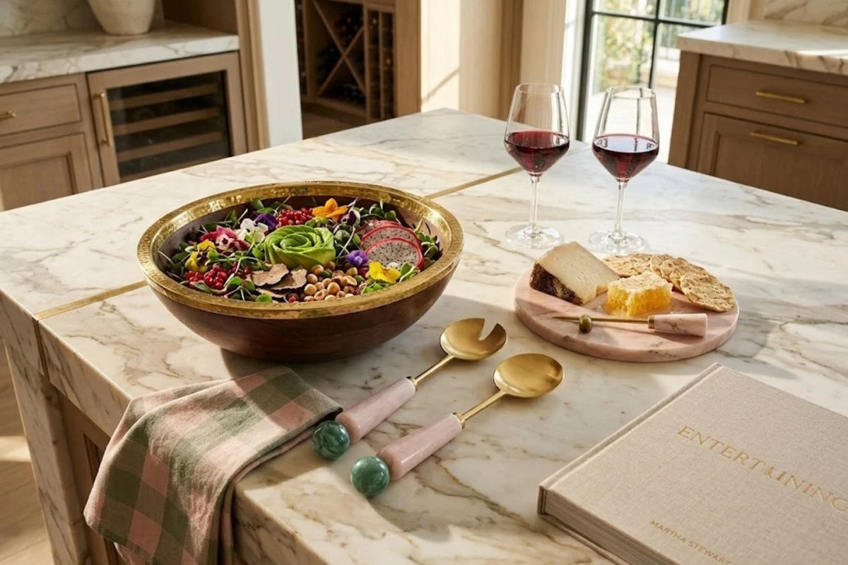 Blush resin salad servers with gold heads resting on a marble island beside a wooden bowl of greens
