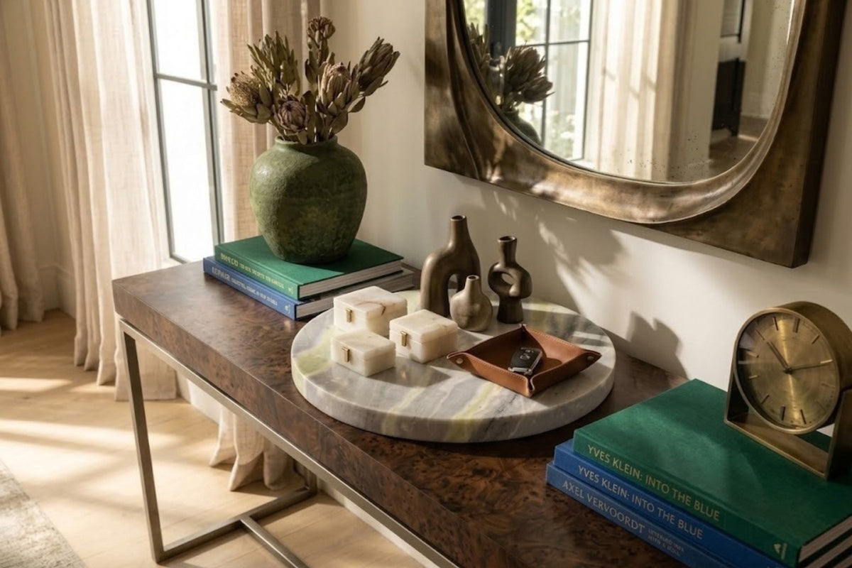 Cream onyx tray with amber banding holding small marble blocks and a leather catchall on a sunlit burl wood console