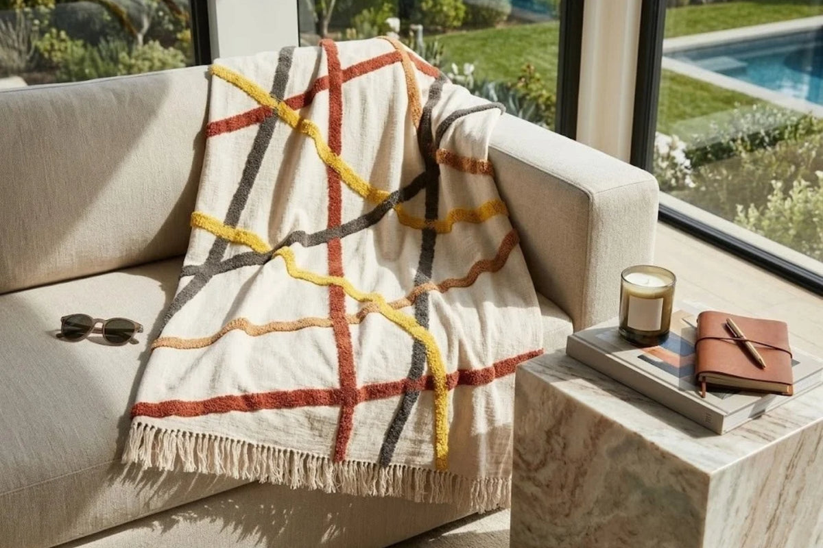 Ivory cotton throw with tufted ochre, red and charcoal lines, draped over a pale sofa beside a stone side table
