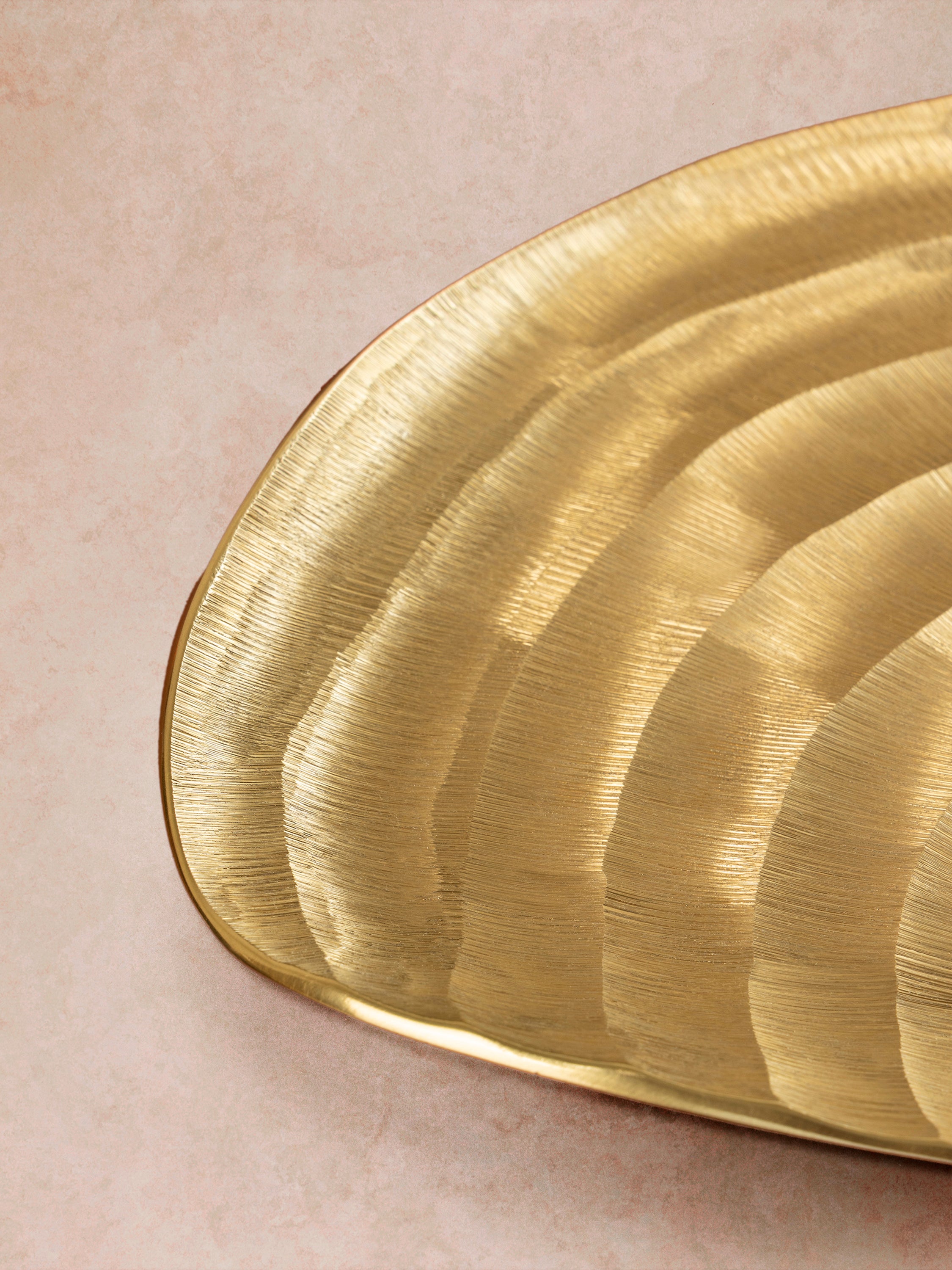 Close-up of gold aluminum tray showing directional ridges, curved edge profile, and subtle variation in the sculpted metallic surface