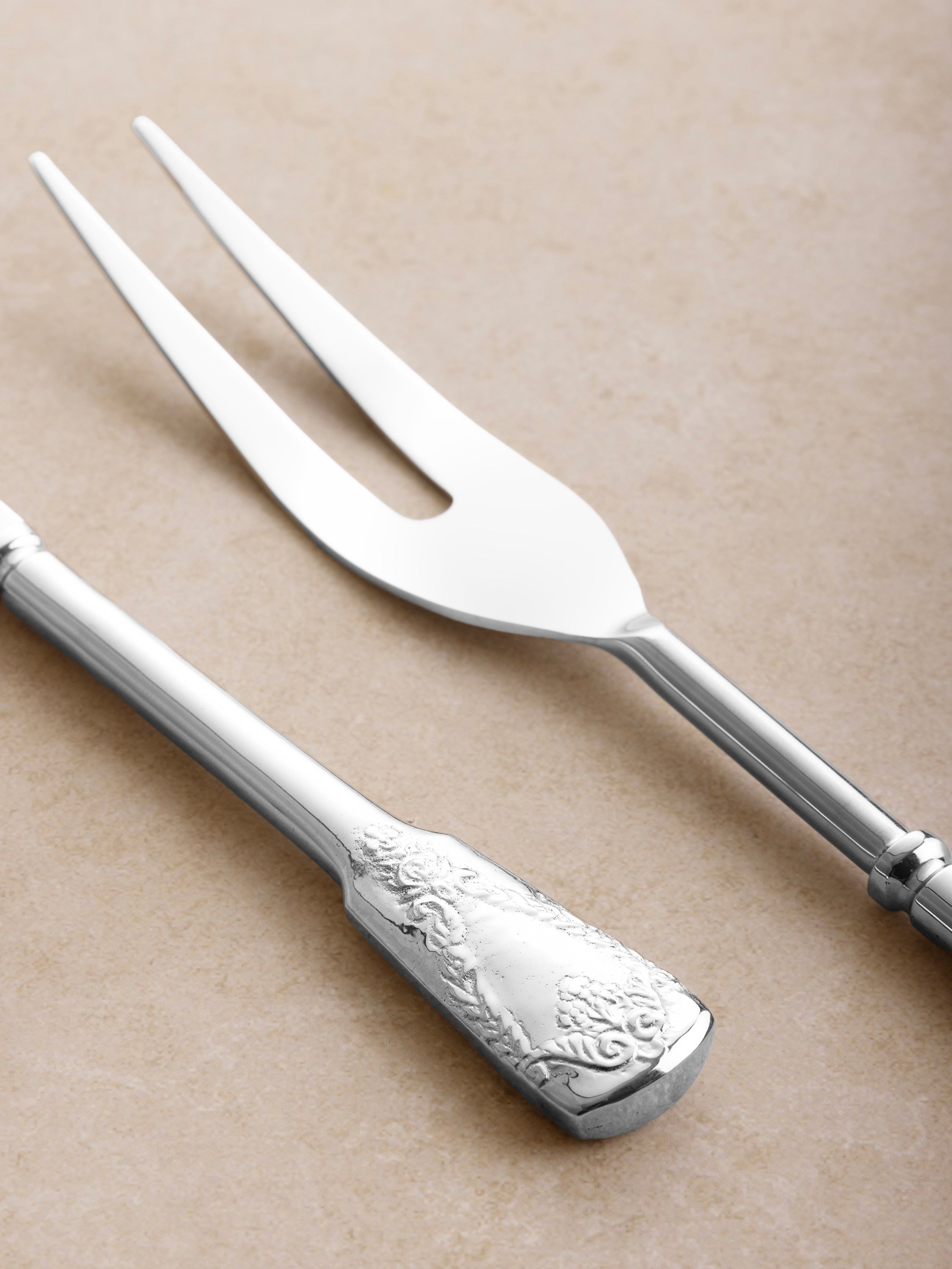 Close-up of carving fork and knife showing sculpted handle detailing, smooth finish, and refined proportions