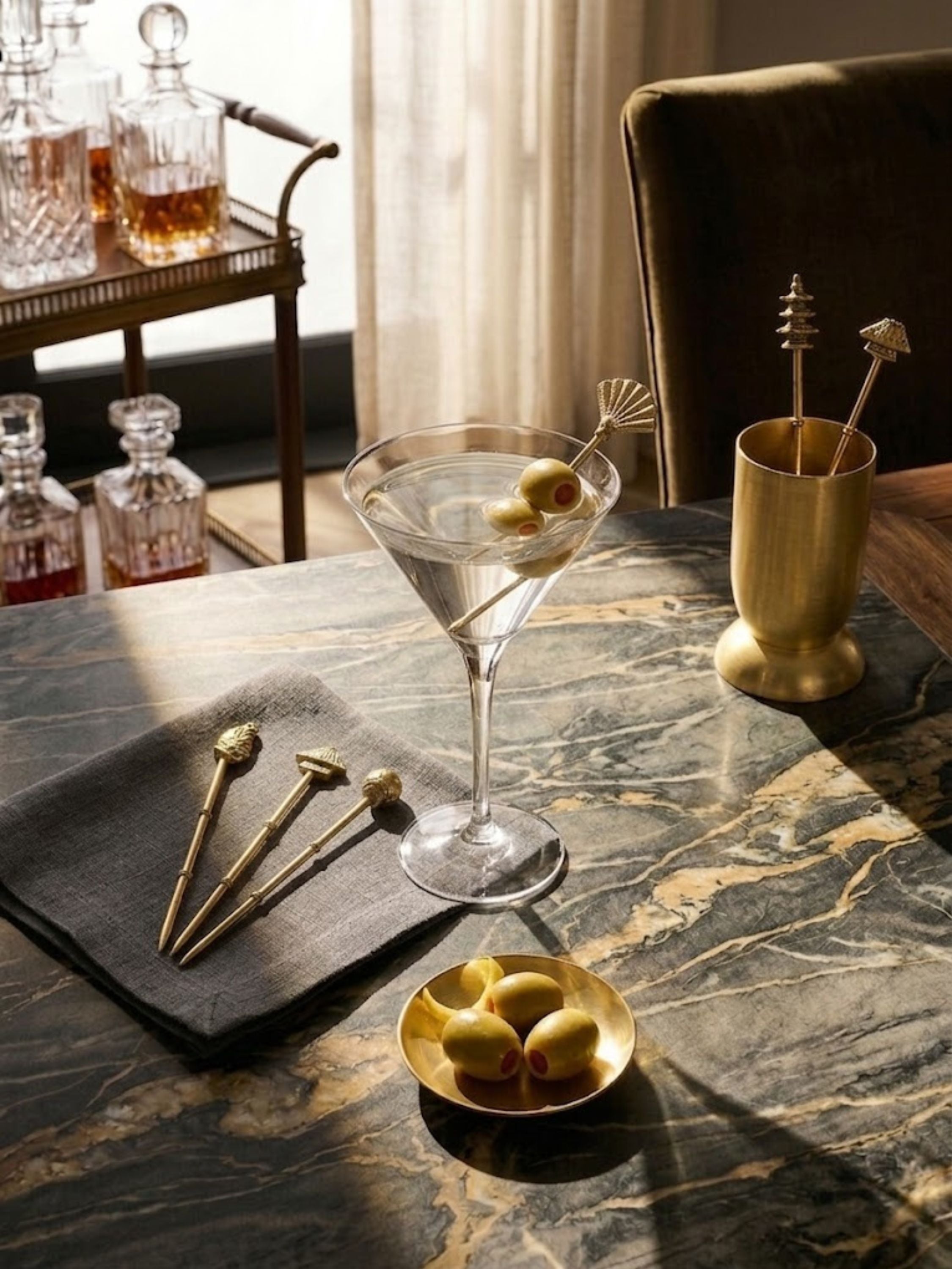 Magnolia gold cocktail picks styled with a classic martini and brass bar accessories, adding a decorative finishing touch to elevated cocktail service and entertaining.