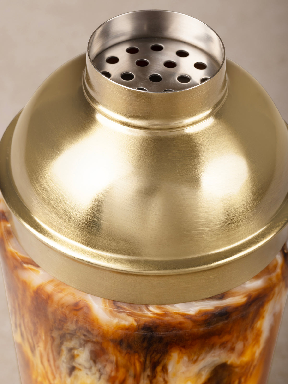 Close-up of the cocktail shaker's matte gold strainer lid and fluid amber pattern in the glossy resin body.