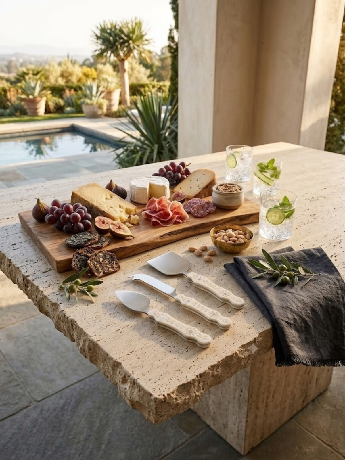 Matte-polished steel cheese knives with ivory carved handles, shown in a poolside setting.