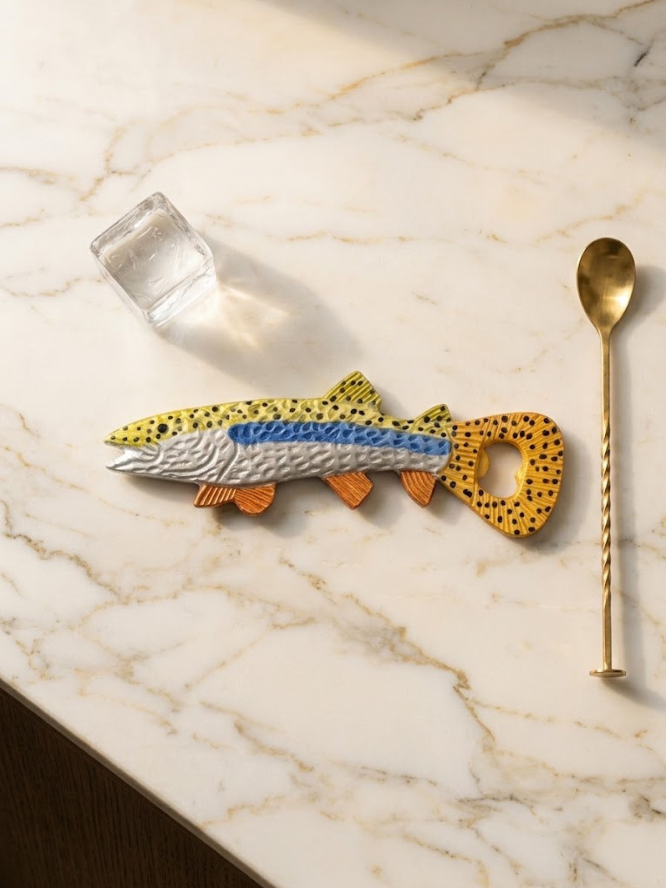 Enamel fish-form bottle opener with burnt orange fins and a black-spotted back, styled on a kitchen counter.