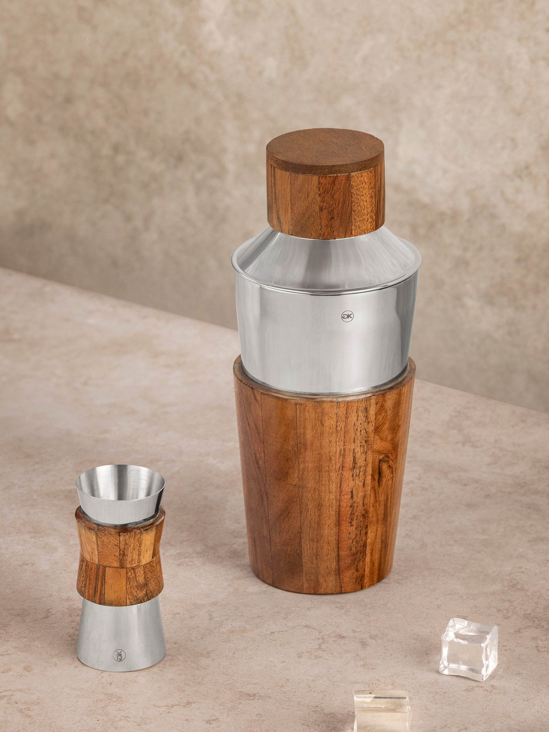 Cocktail shaker and jigger set in stainless steel with handcrafted wood components, shown in a clean top-down composition