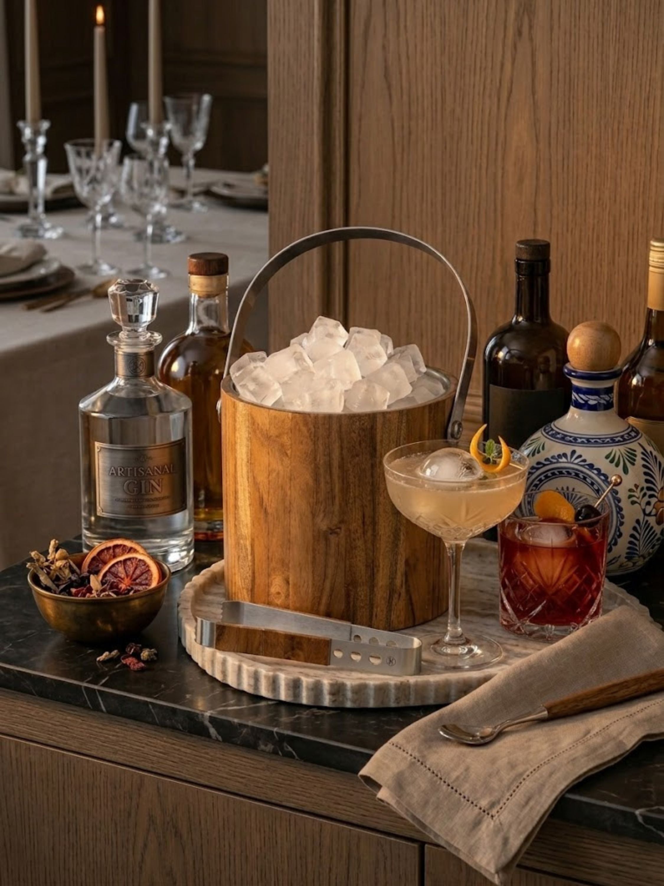 Chicago Ice Bucket styled for whiskey service on a marble bar, featuring a handcrafted wooden exterior with stainless steel liner, matching lid, and ice tongs for sophisticated entertaining.