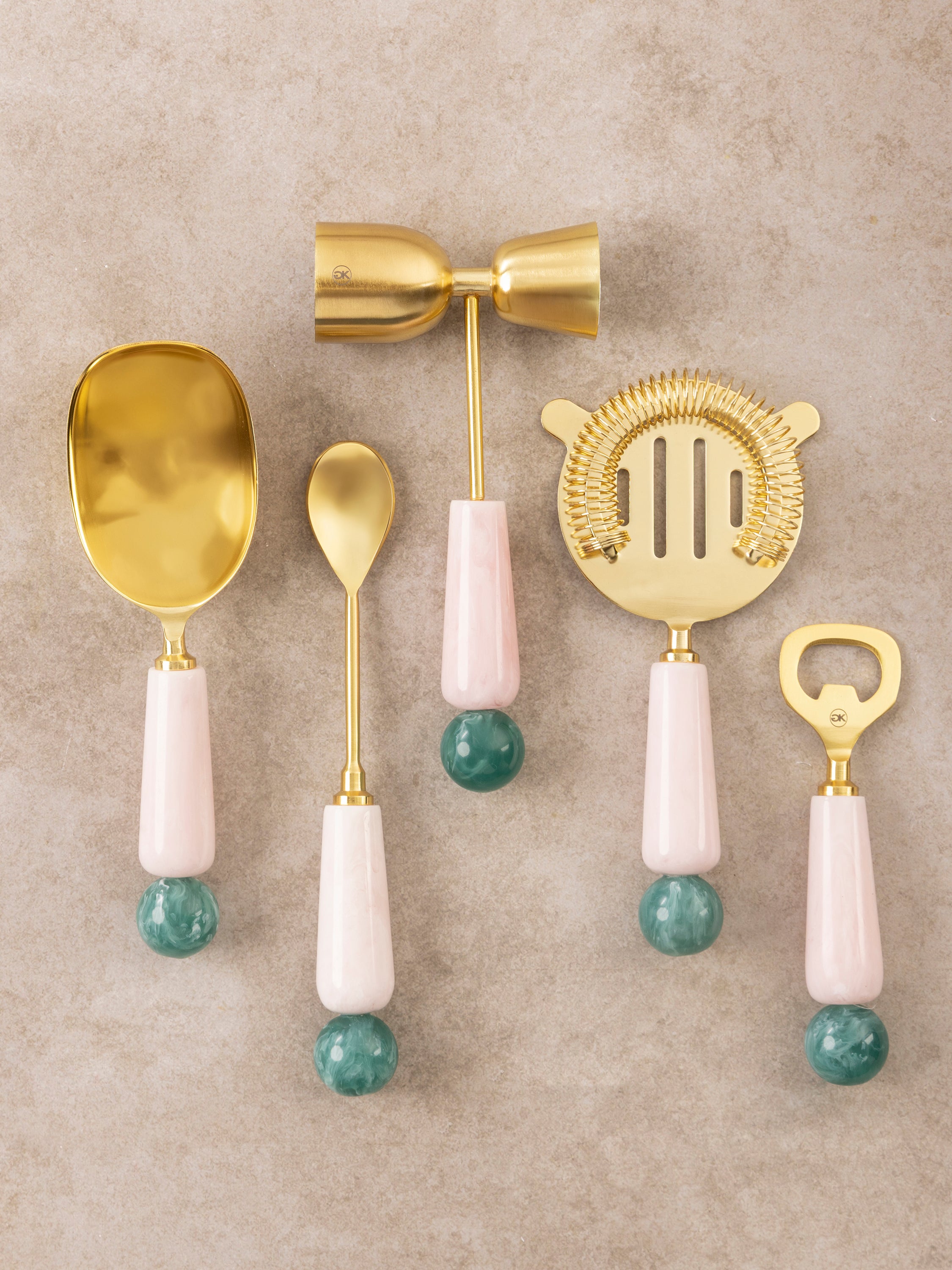 Bar tools set with brass-toned utensils and sculpted resin handles shown in a clean top-down composition