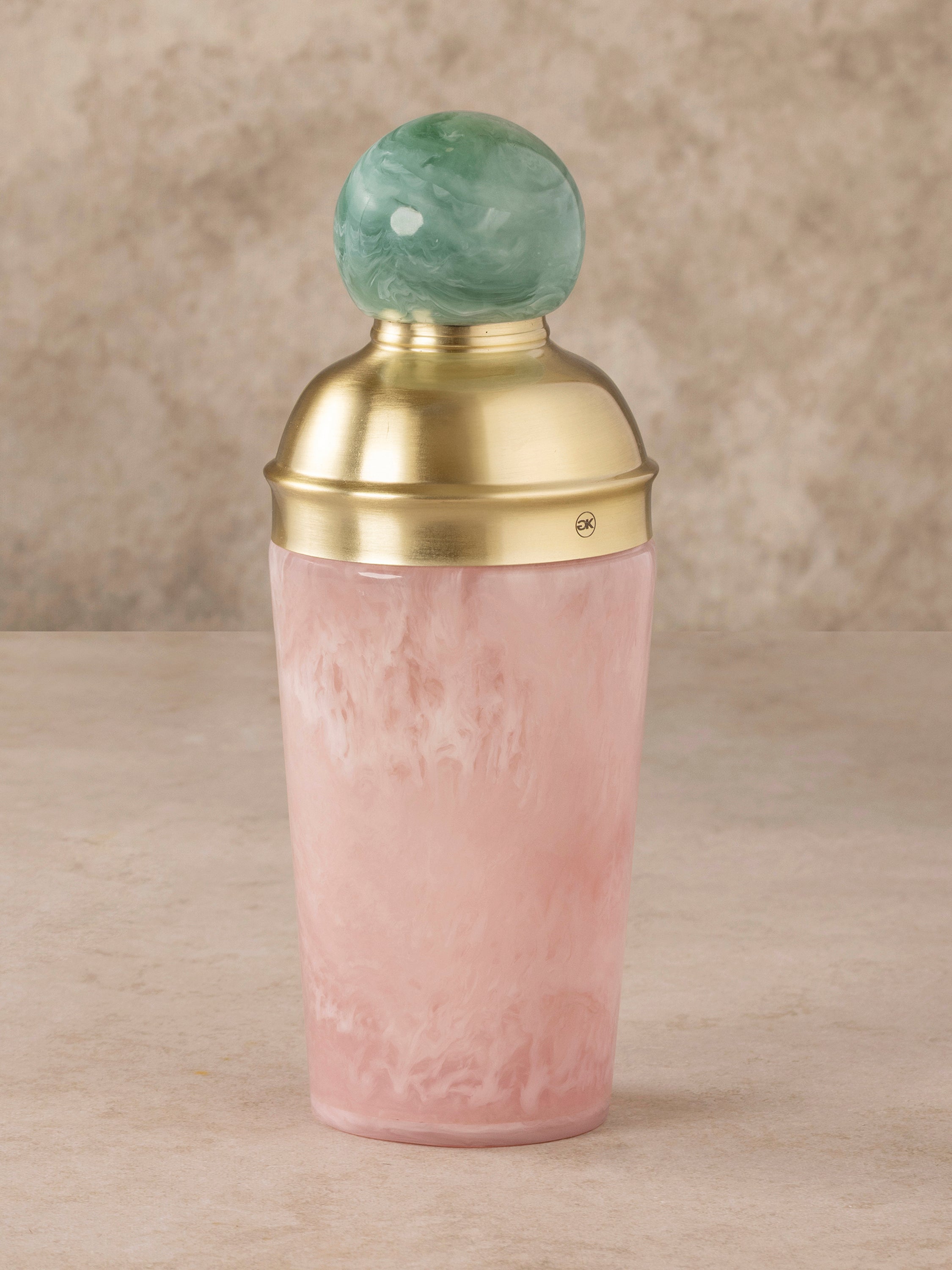 Marbled resin cocktail shaker with blush tones and brass lid with green knob finial, shown in a clean front-facing composition