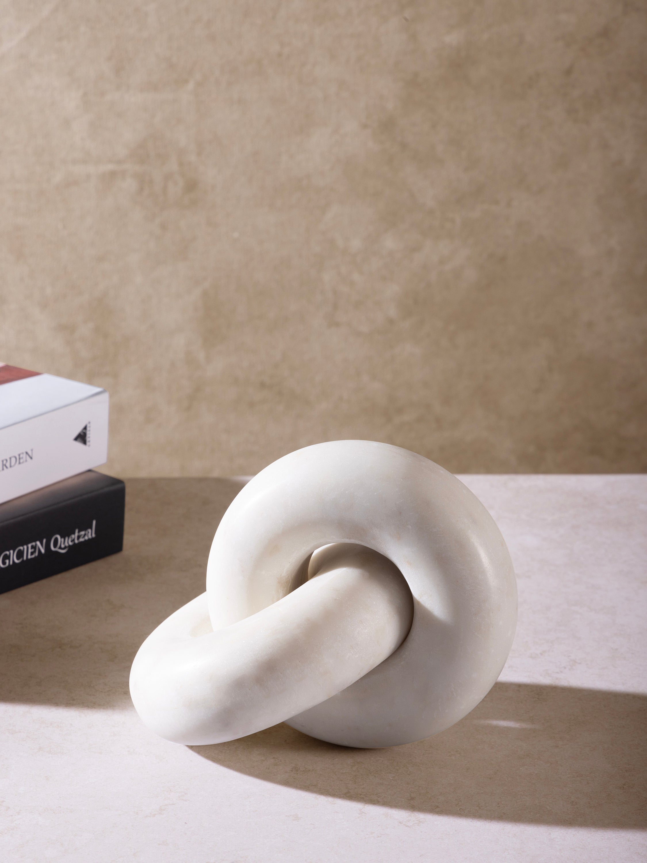 White marble knot sculpture placed on a surface beside stacked books, highlighting compact scale and sculptural form