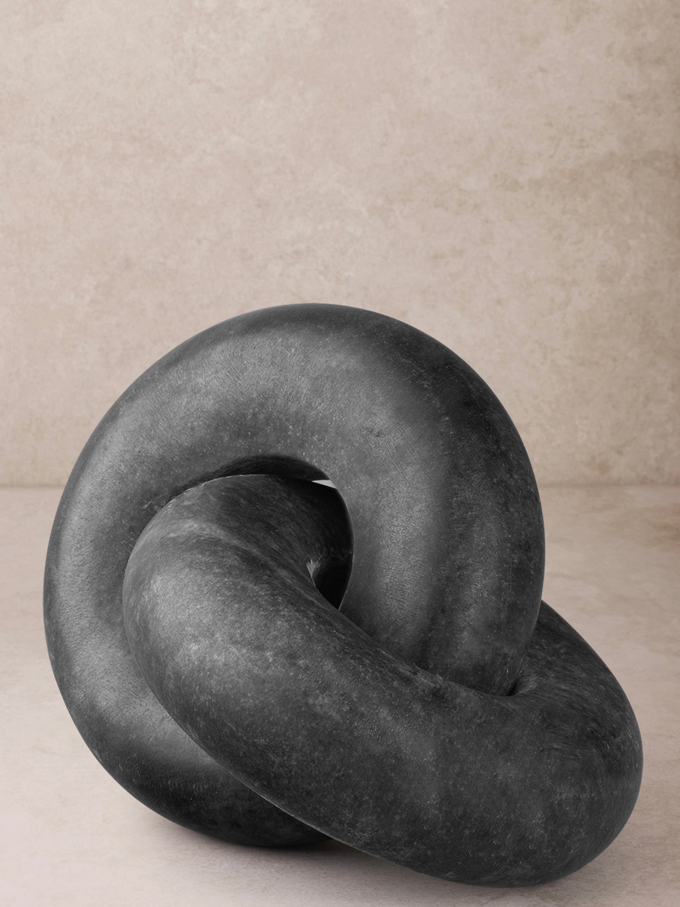 Sculpted marble knot in deep black stone with interlocking curved form and matte polished surface, shown in a clean front-facing composition
