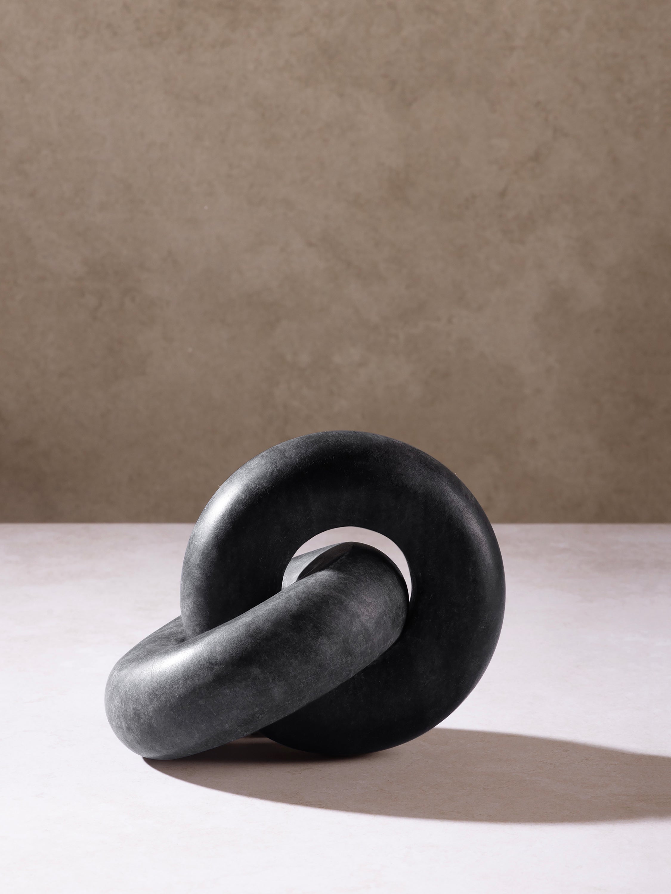 Black marble knot sculpture placed on a surface, highlighting compact form and sculptural weight