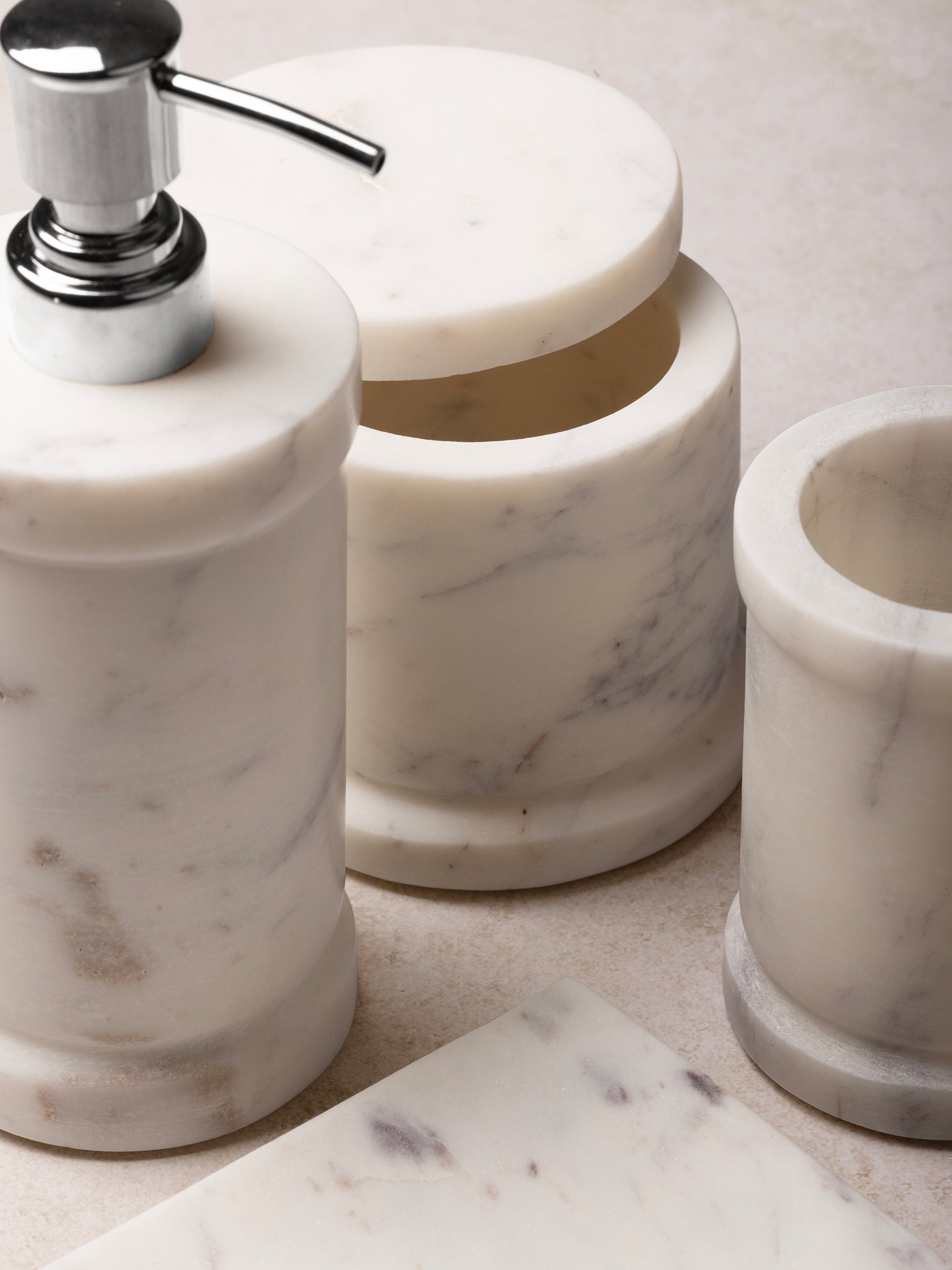 Close-up of marble dispenser and accessories showing cylindrical forms, polished finish, and soft natural veining