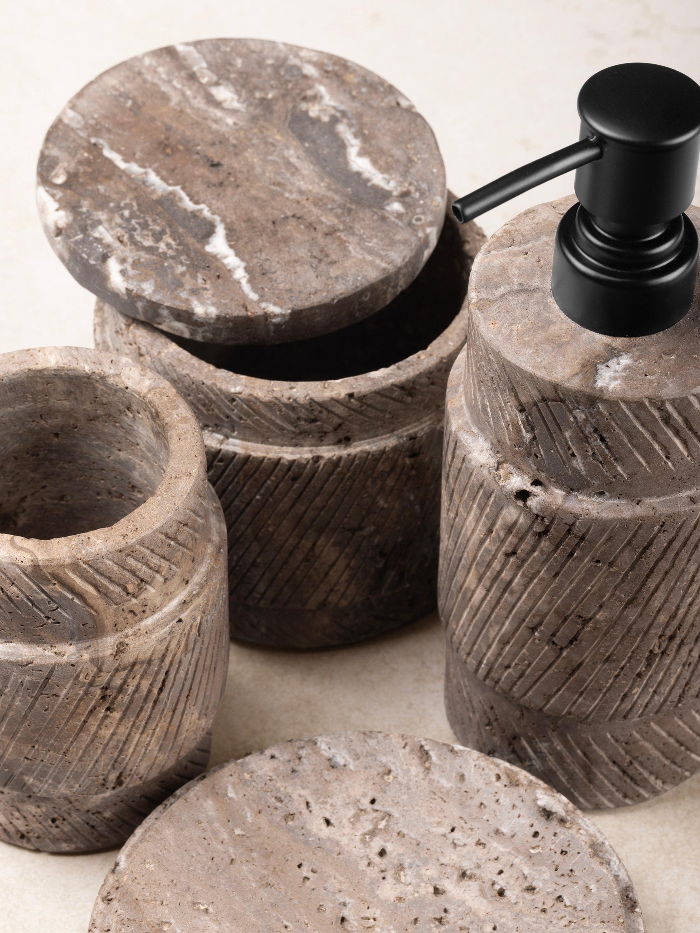 Close-up of the Tallinn travertine accessories showing cylindrical forms, porous stone texture, and natural variation in gray and beige tones.
