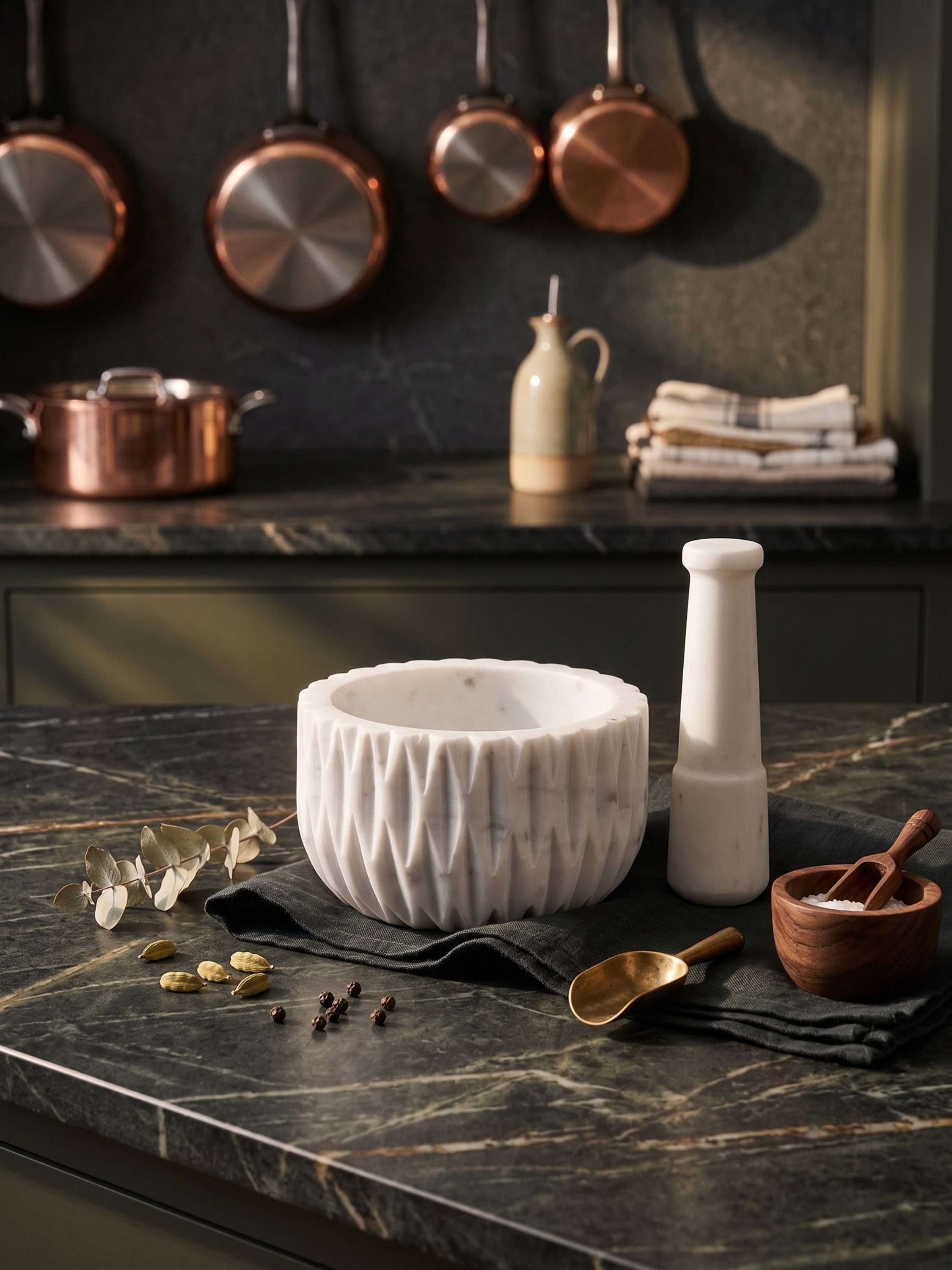 Fluted white marble mortar and pestle filled with whole spices, set on a dark kitchen counter near glass jars and a window-lit pantry setting