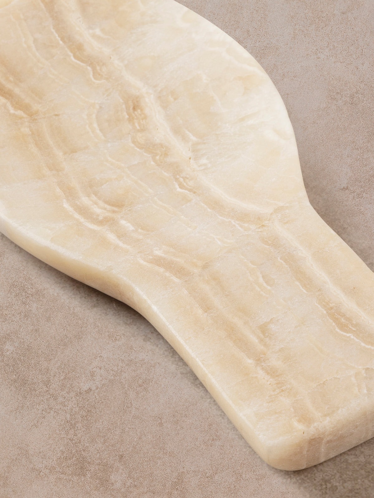 Machu Picchu onyx spoon rest shown at an angle, honey banding running the length of the cream stone.