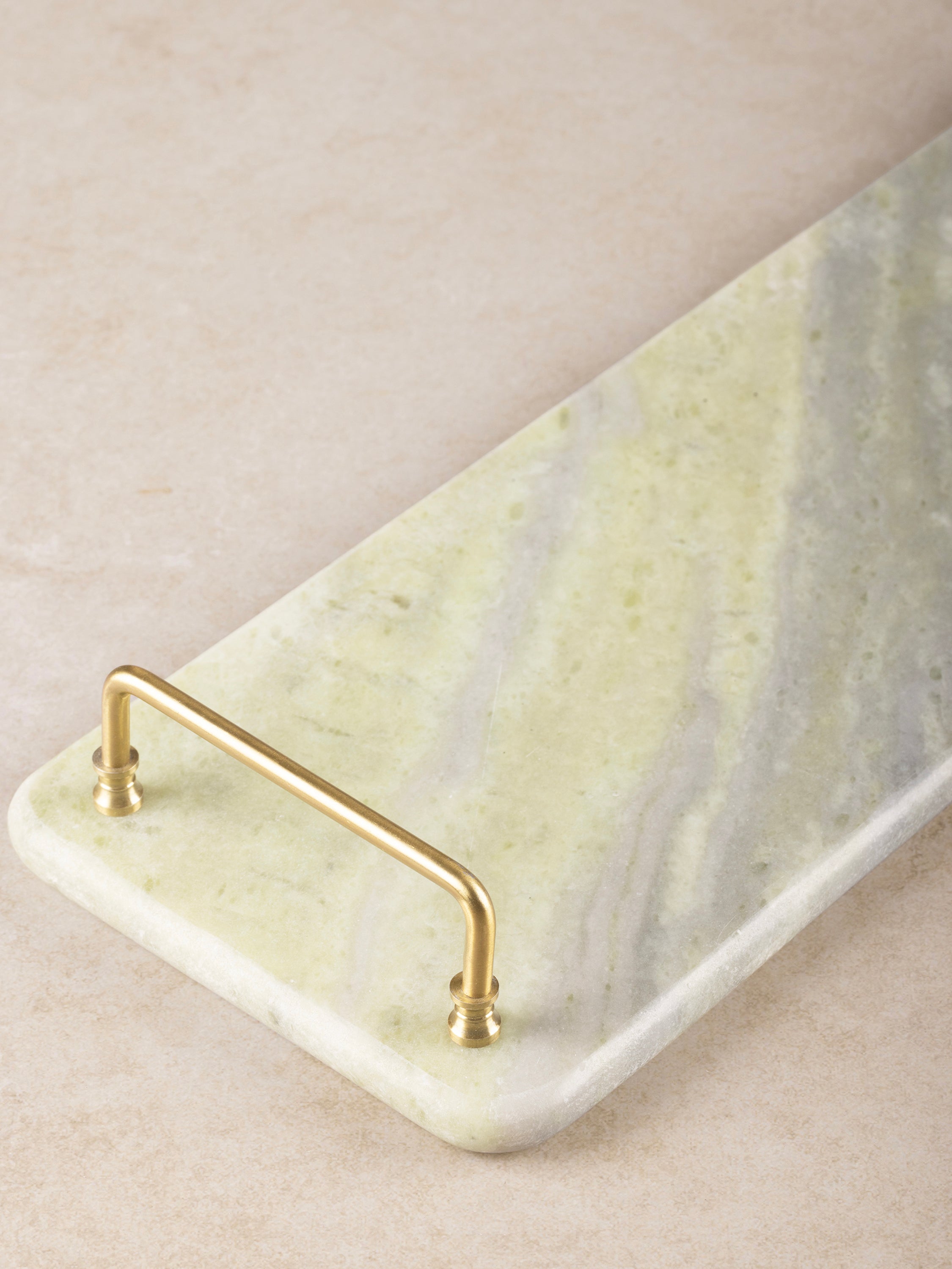 Close-up of onyx tray corner showing brass handle detail, polished stone surface, and soft green veining