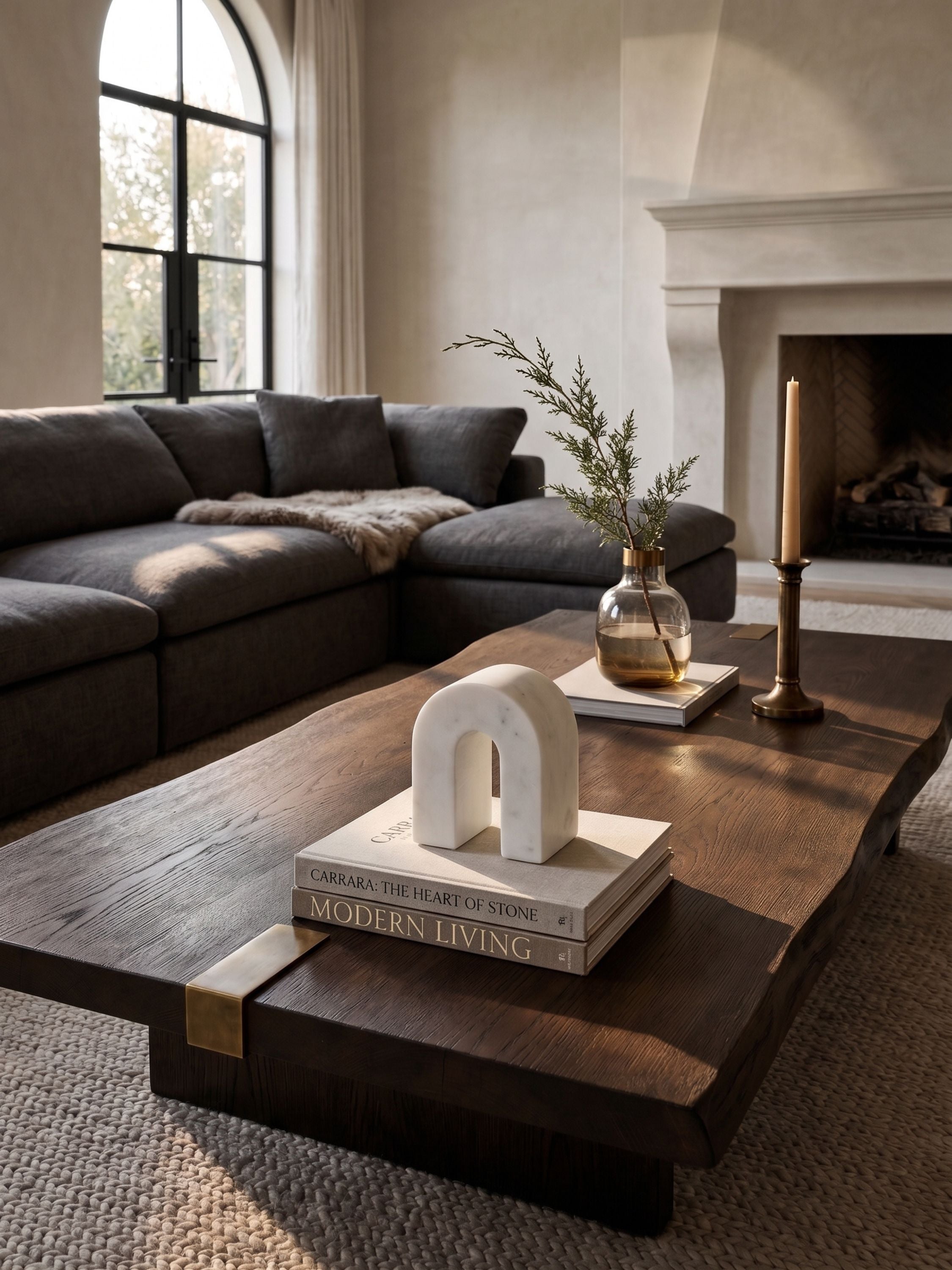 Marble arch sculpture styled on a coffee table with books, candle, and vase in a living room setting