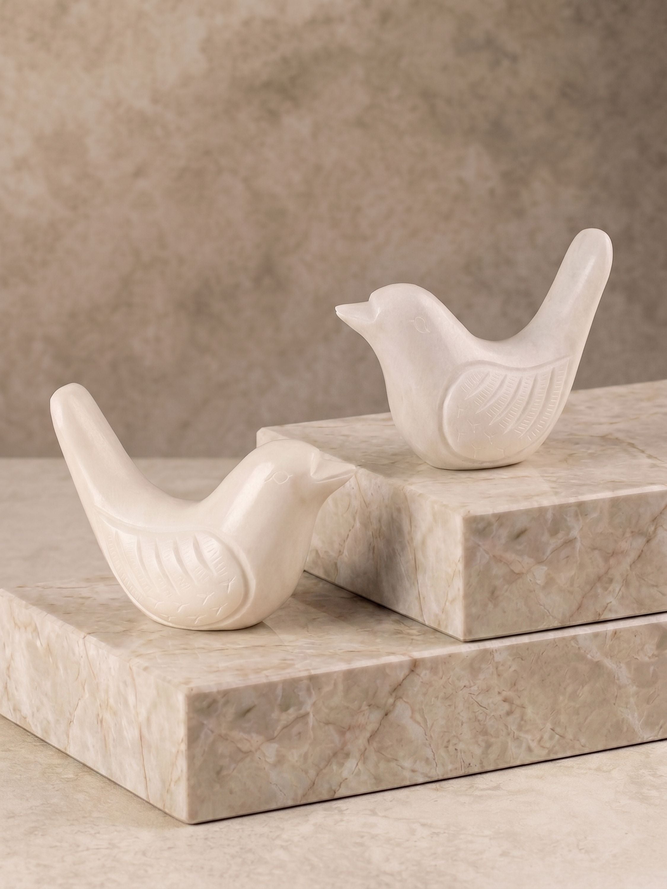 White marble bird figurines set of two displayed on stacked stone blocks against a neutral background