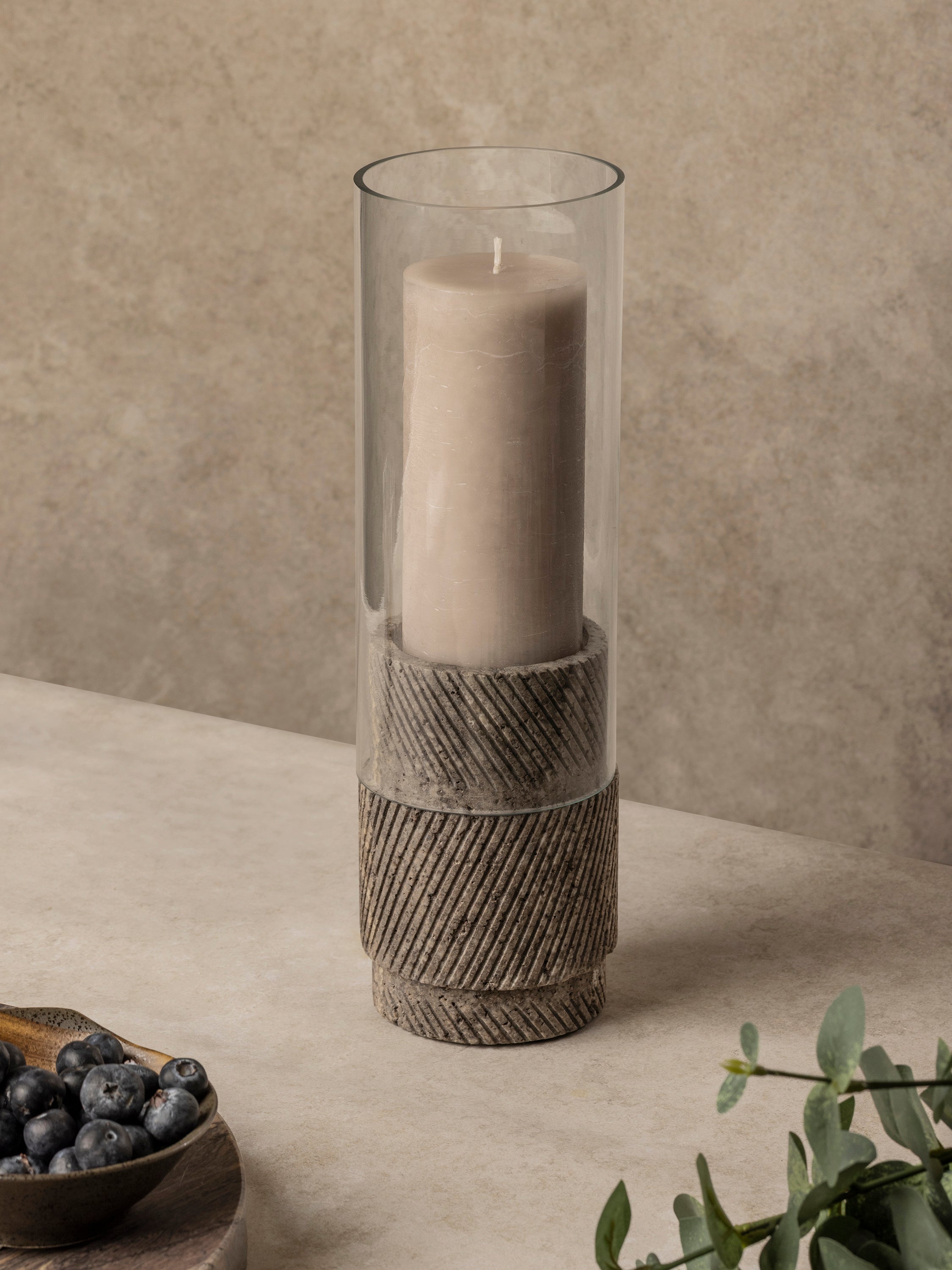 Brown travertine hurricane candle holder with cylindrical glass insert and carved stone base, shown in a clean front-facing composition