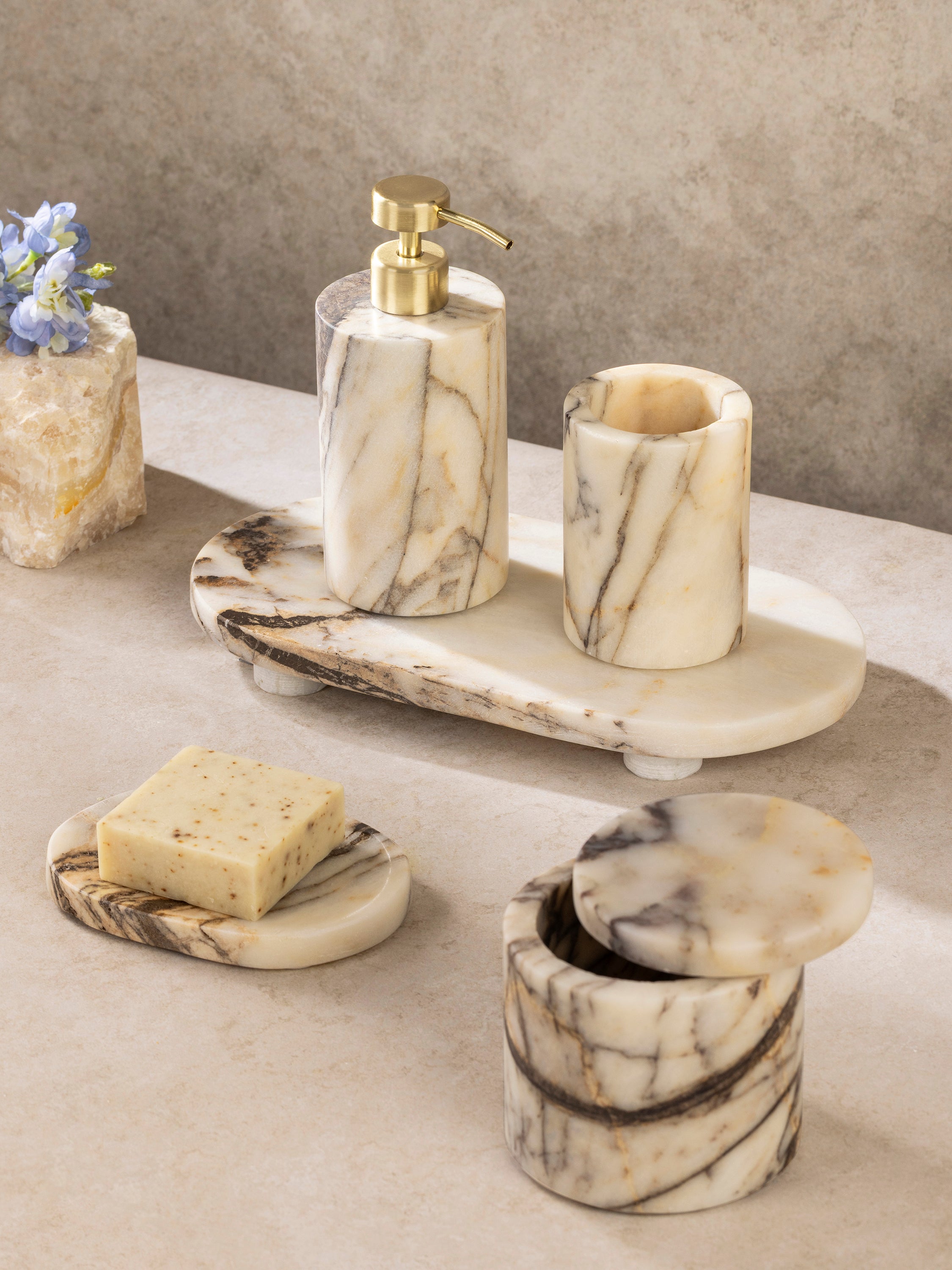 Marble bath accessories set with soap dispenser, toothbrush holder, and tray in warm stone tones, shown in a clean front-facing composition