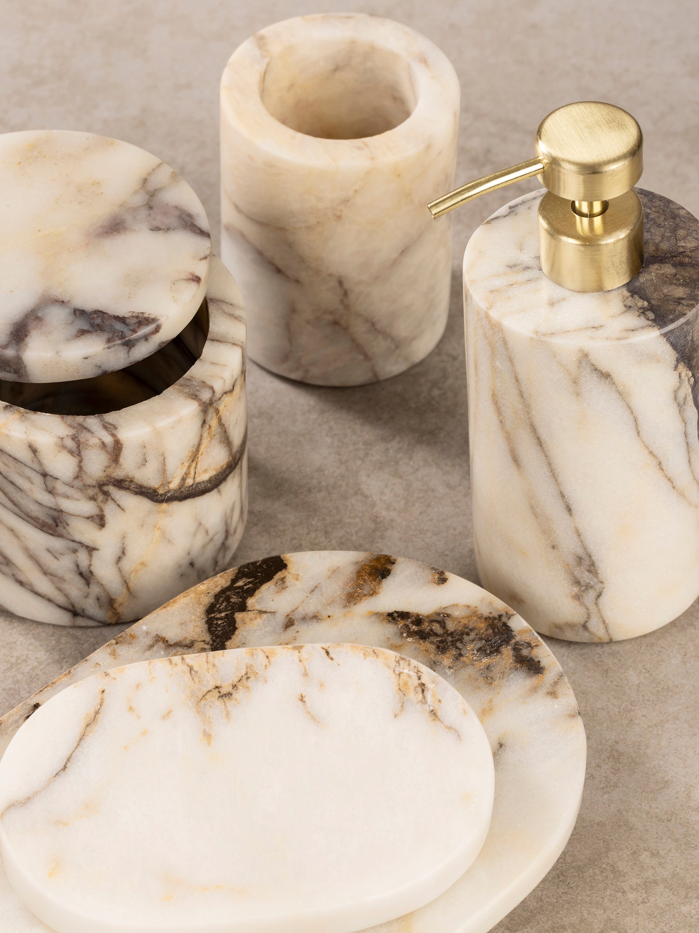 Close-up of Tangier bath set components showing soap dish, dispenser pump, and container with natural stone surface variation