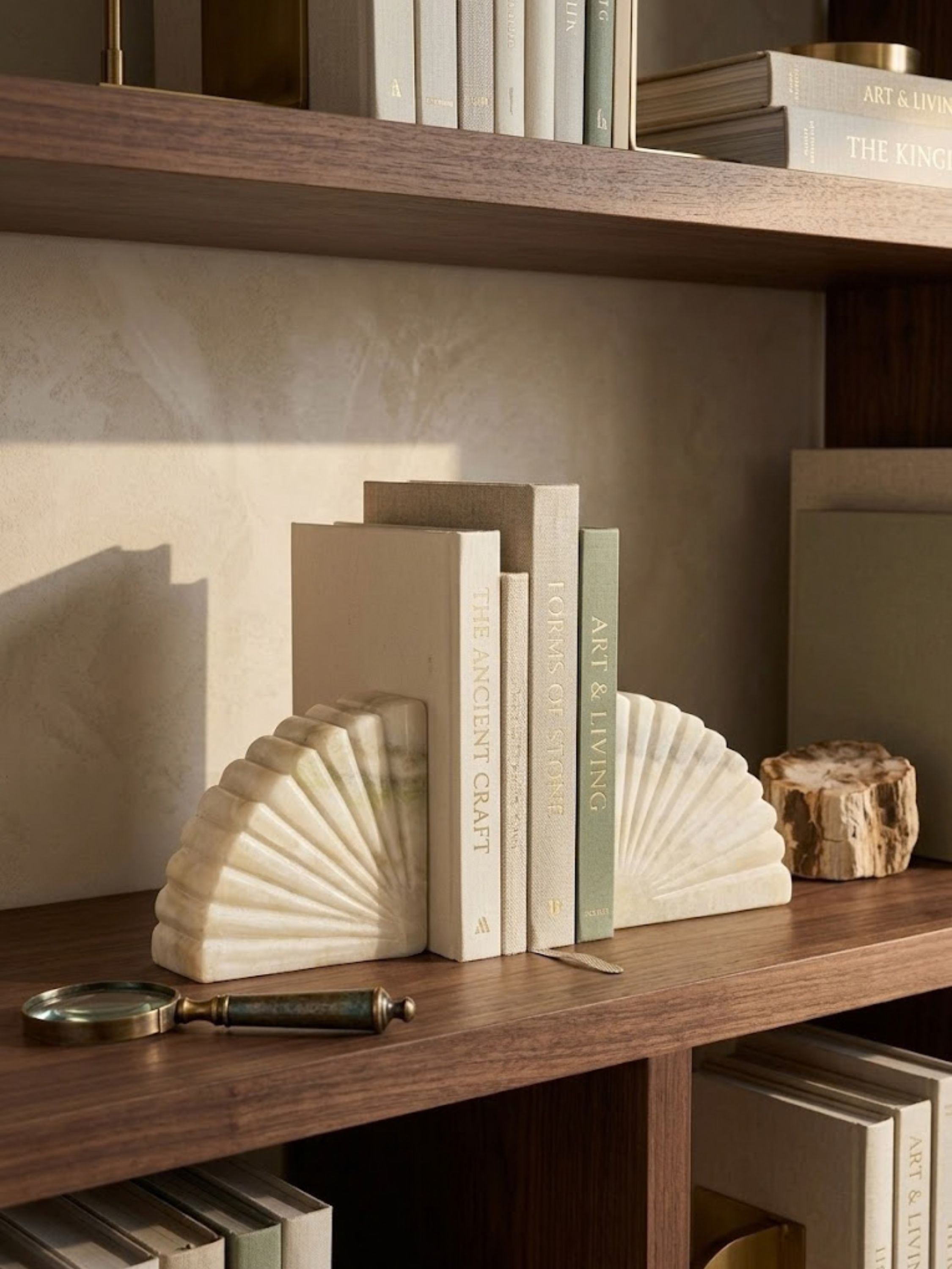 Emrys onyx bookends styled on a warm wood bookshelf, their fan-inspired forms set among a library display.
