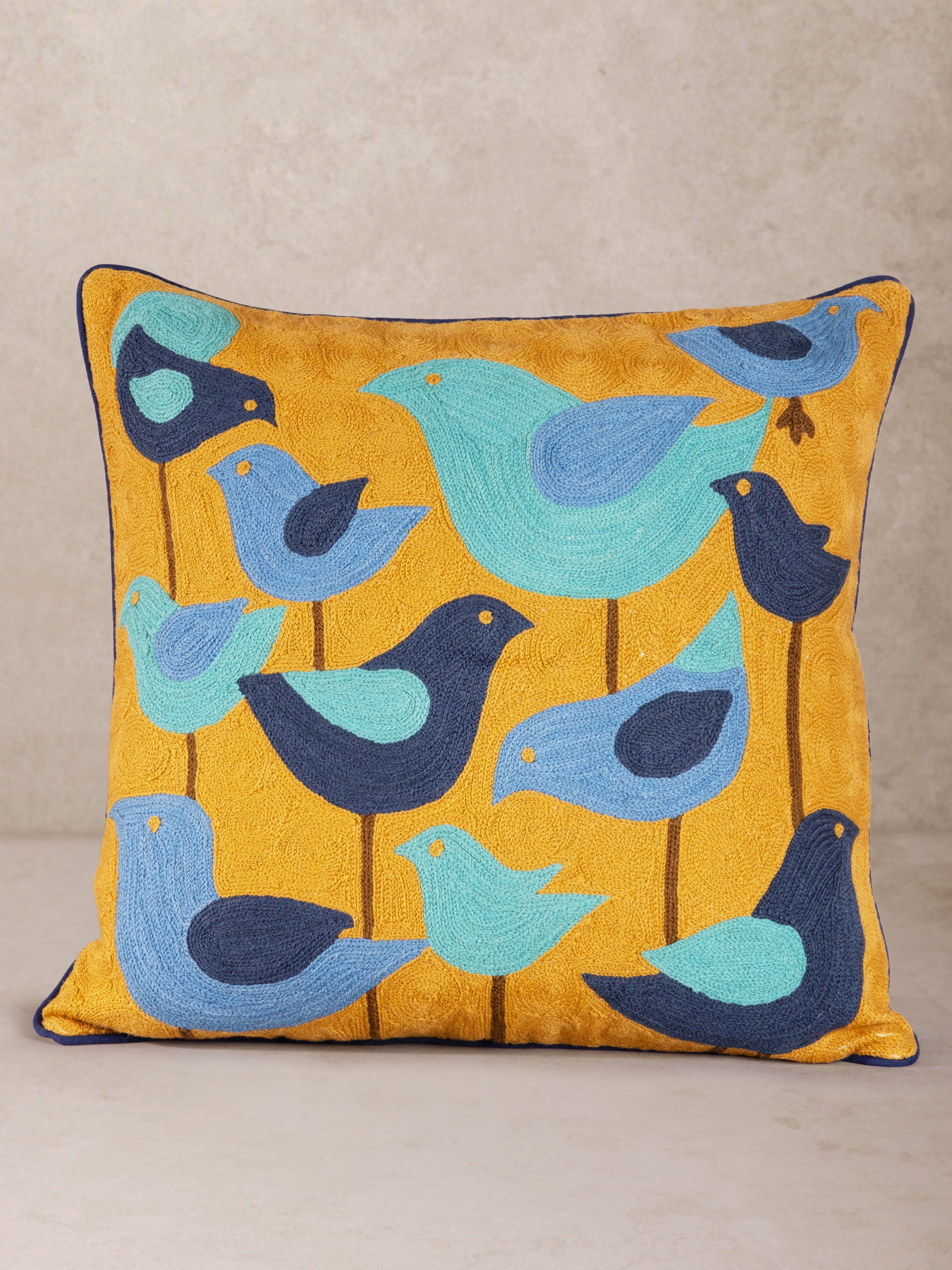 Whimsical embroidered throw pillow featuring a charming flock of blue and navy birds on a warm mustard yellow background