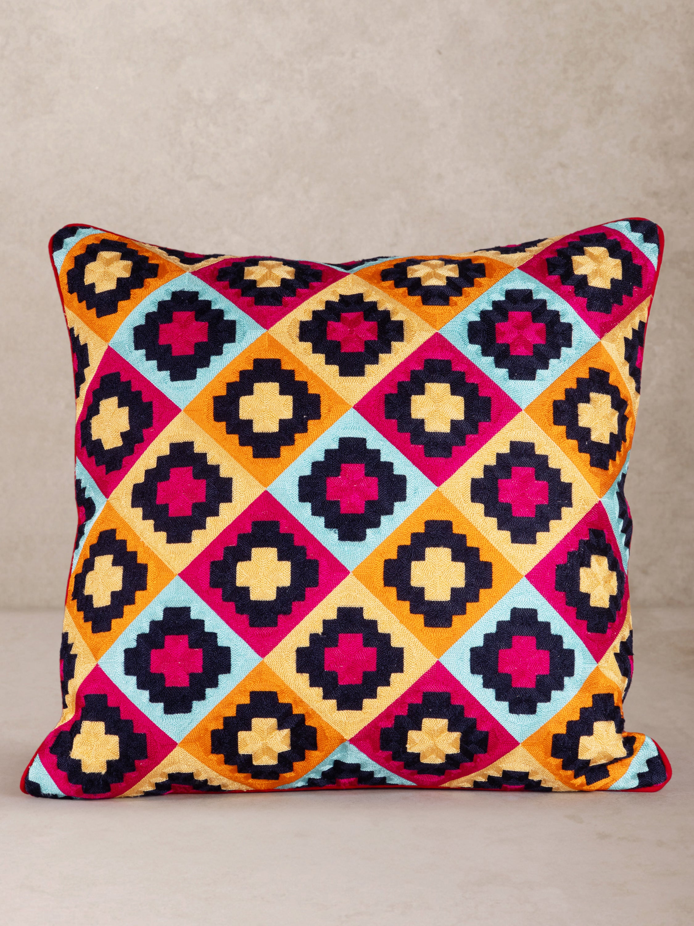 Handcrafted natural cotton throw pillow with bold geometric embroidery in red, blue, orange and black — artisan luxury accent