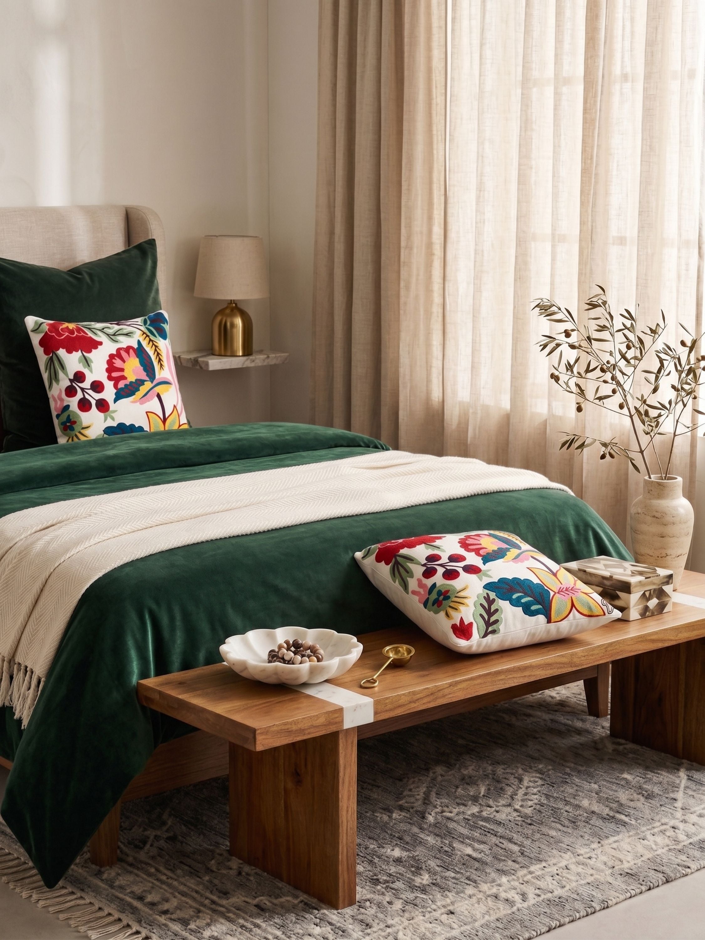 Hand embroidered folk floral pillow cover in vibrant multicolor tones styled on a bed with deep green bedding in a warm, softly lit bedroom setting