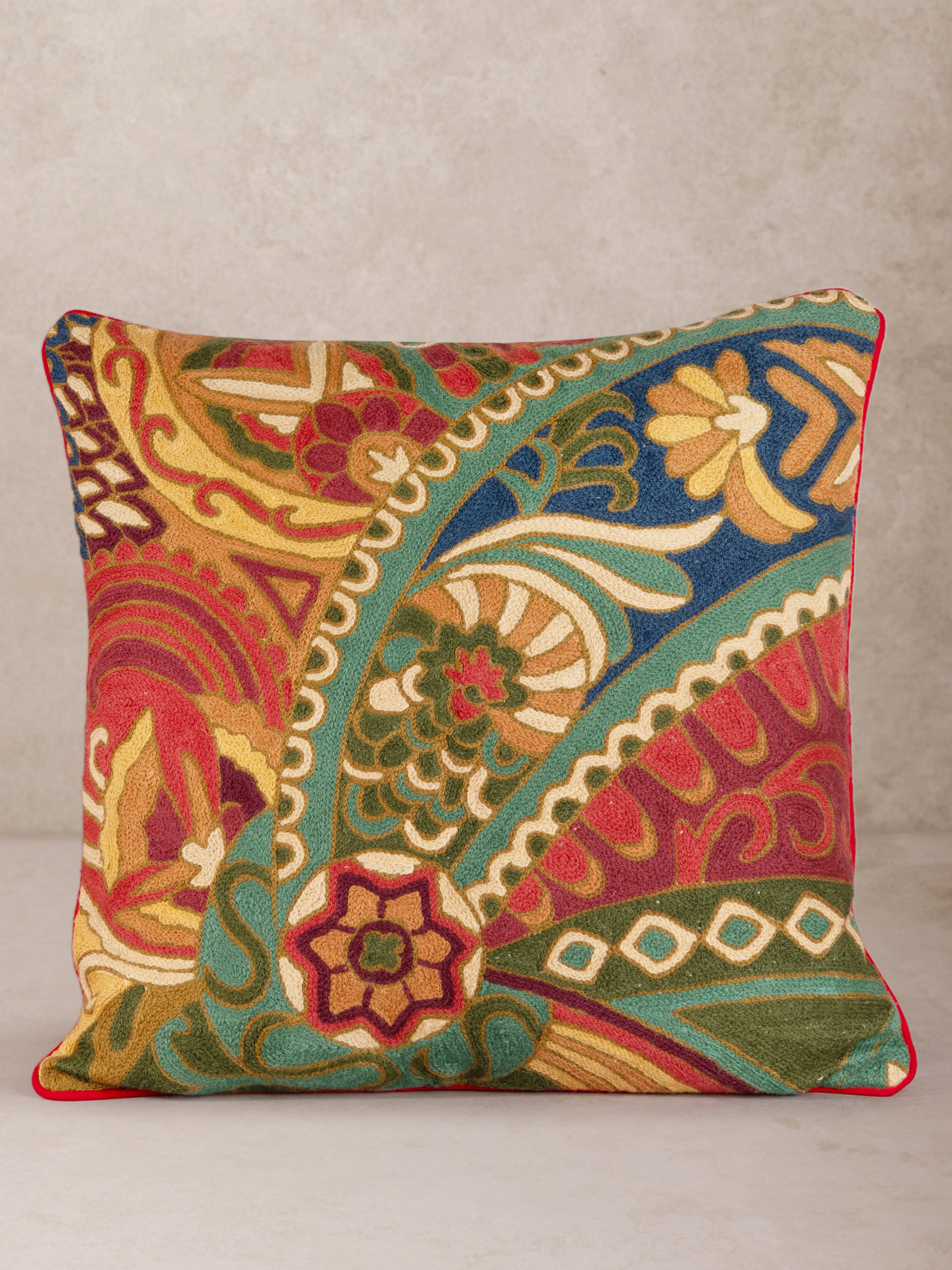 Elegant embroidered throw pillow featuring a rich paisley and floral design in warm tones of red, green, gold, and blue