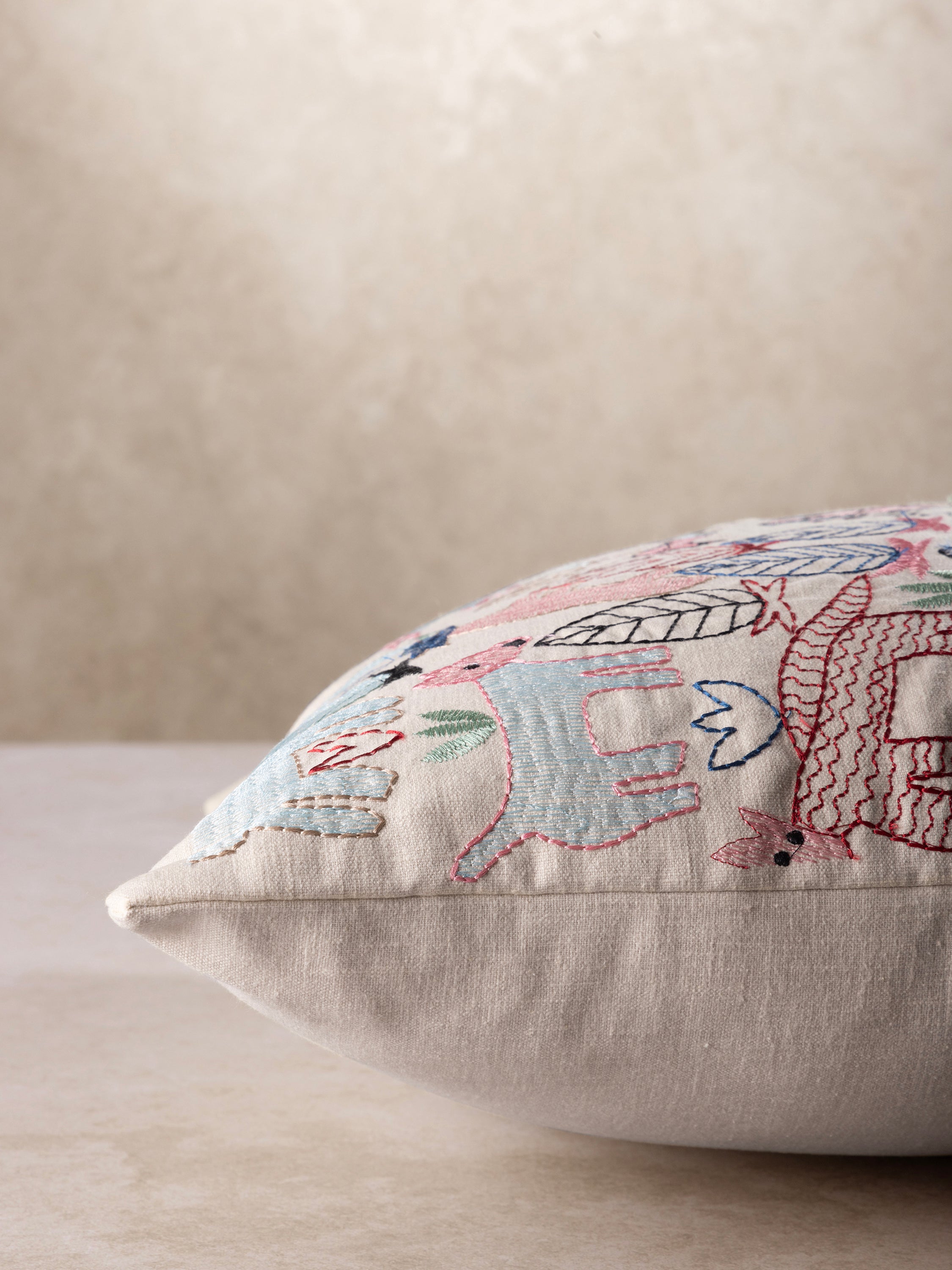 Artisan-made decorative pillow in cotton featuring playful embroidered animal scenes and botanical detail — luxury home layer