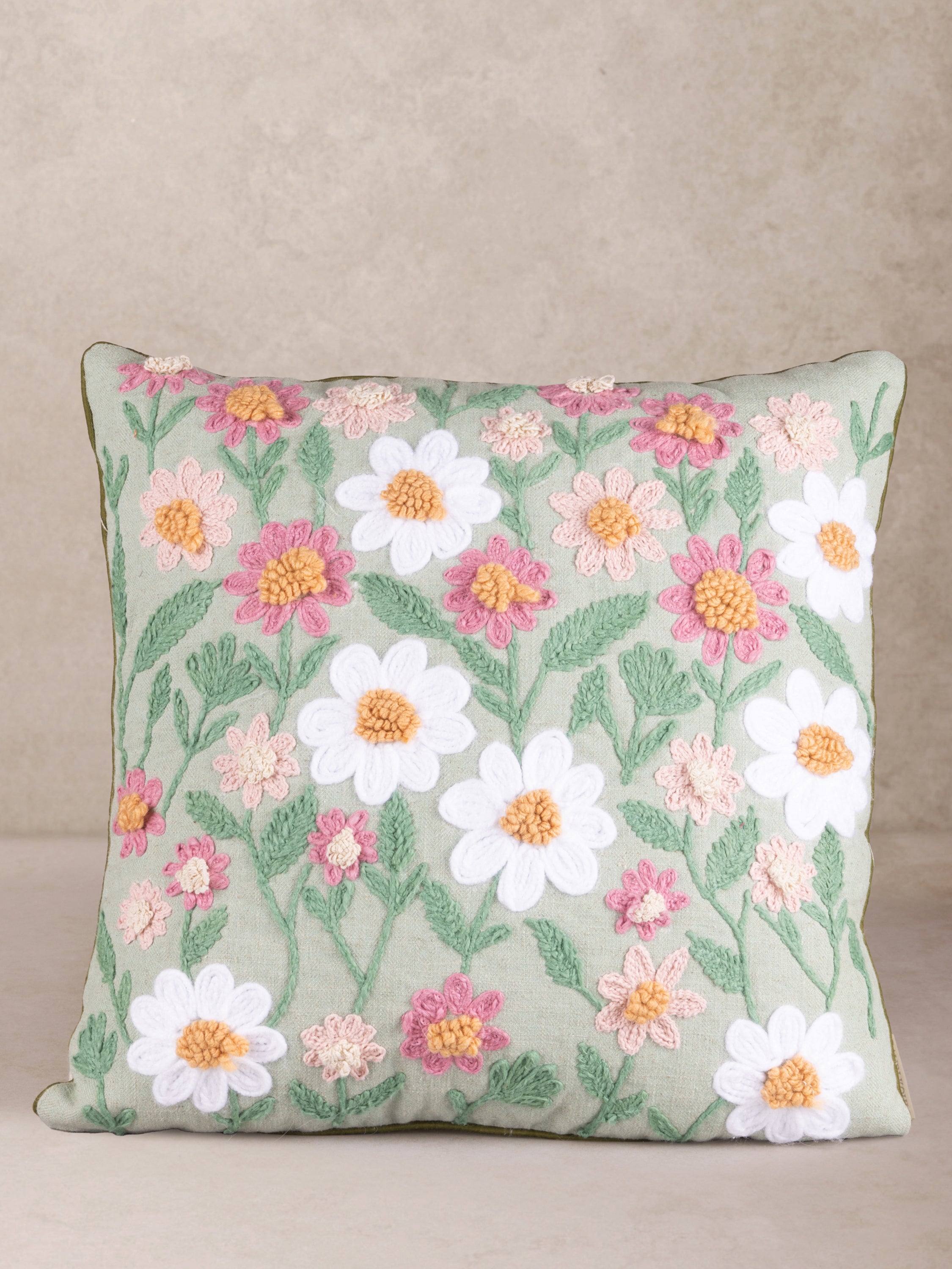 Handcrafted cotton throw pillow with soft white and blush embroidered daisies on sage background — artisan luxury accent