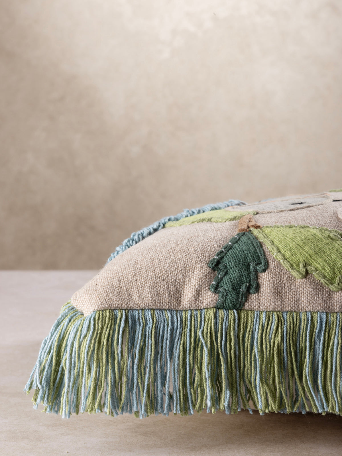 Side profile of the throw pillow showing its plush fill and fringe trim along the seam.