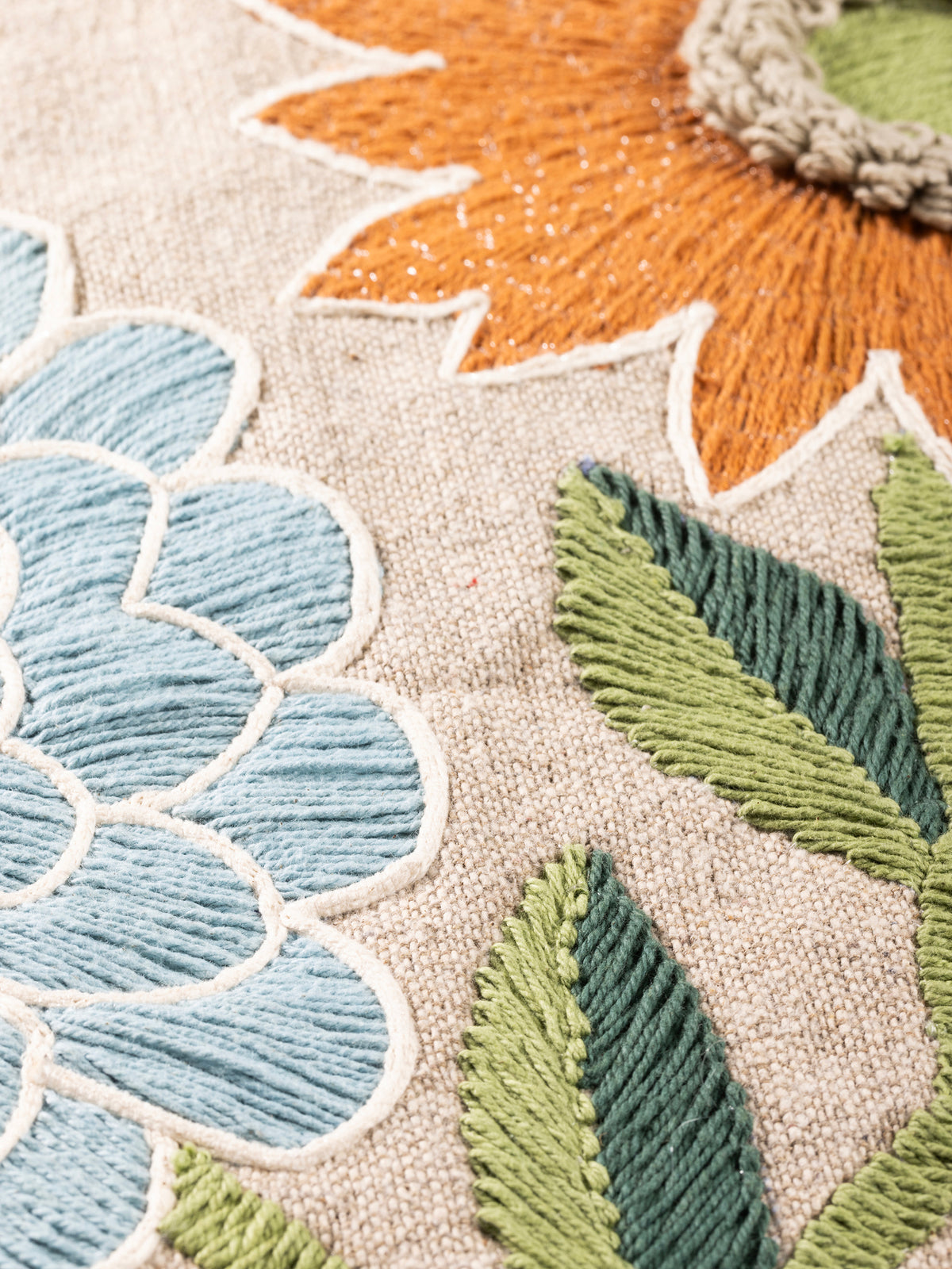 Close-up of the embroidered blossoms showing raised stitchwork in terracotta, olive, and blue tones.