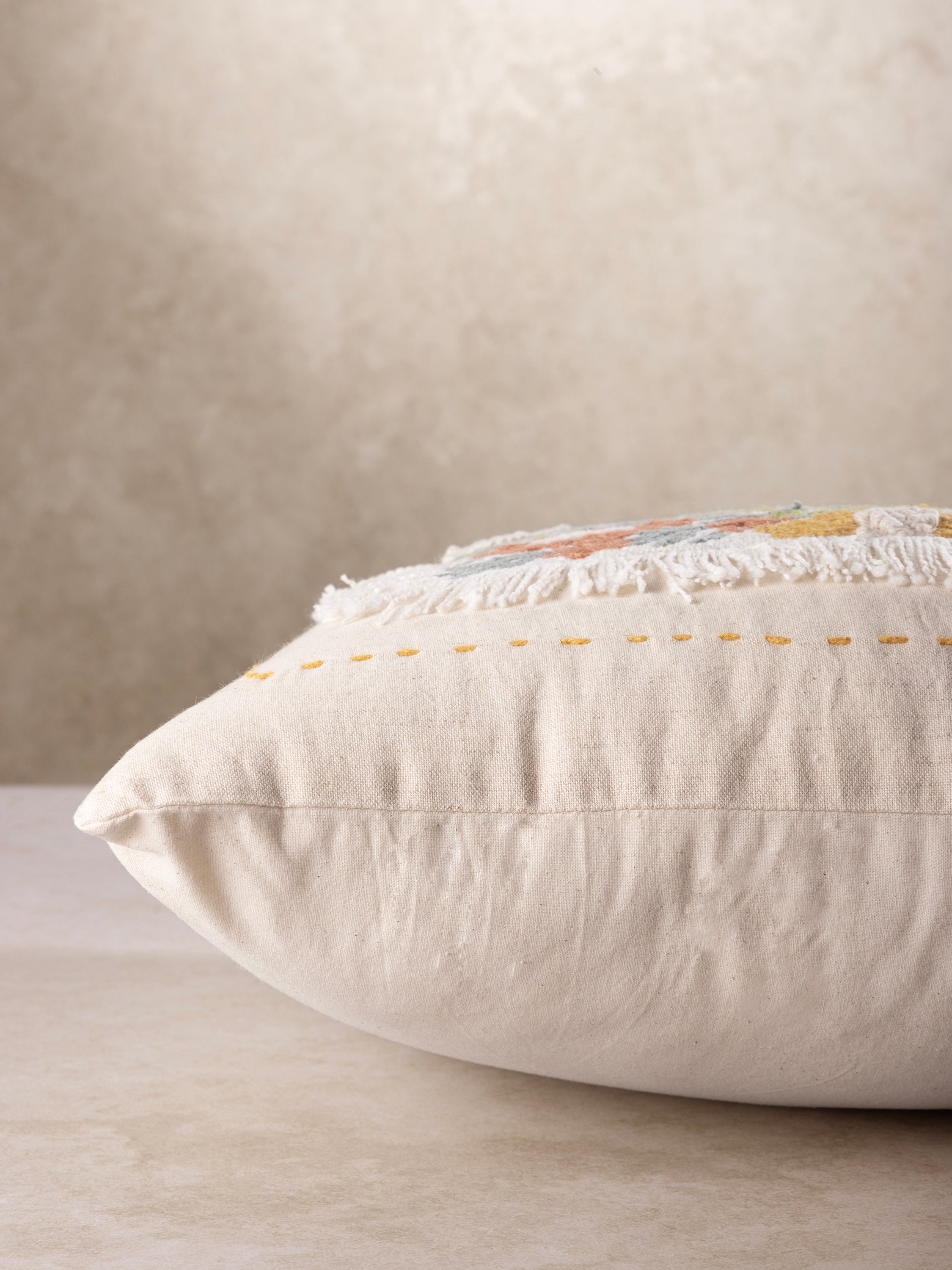 Side profile of the Perth throw pillow showing its plush filled structure, soft rounded edges, and fringe trim along the seam.