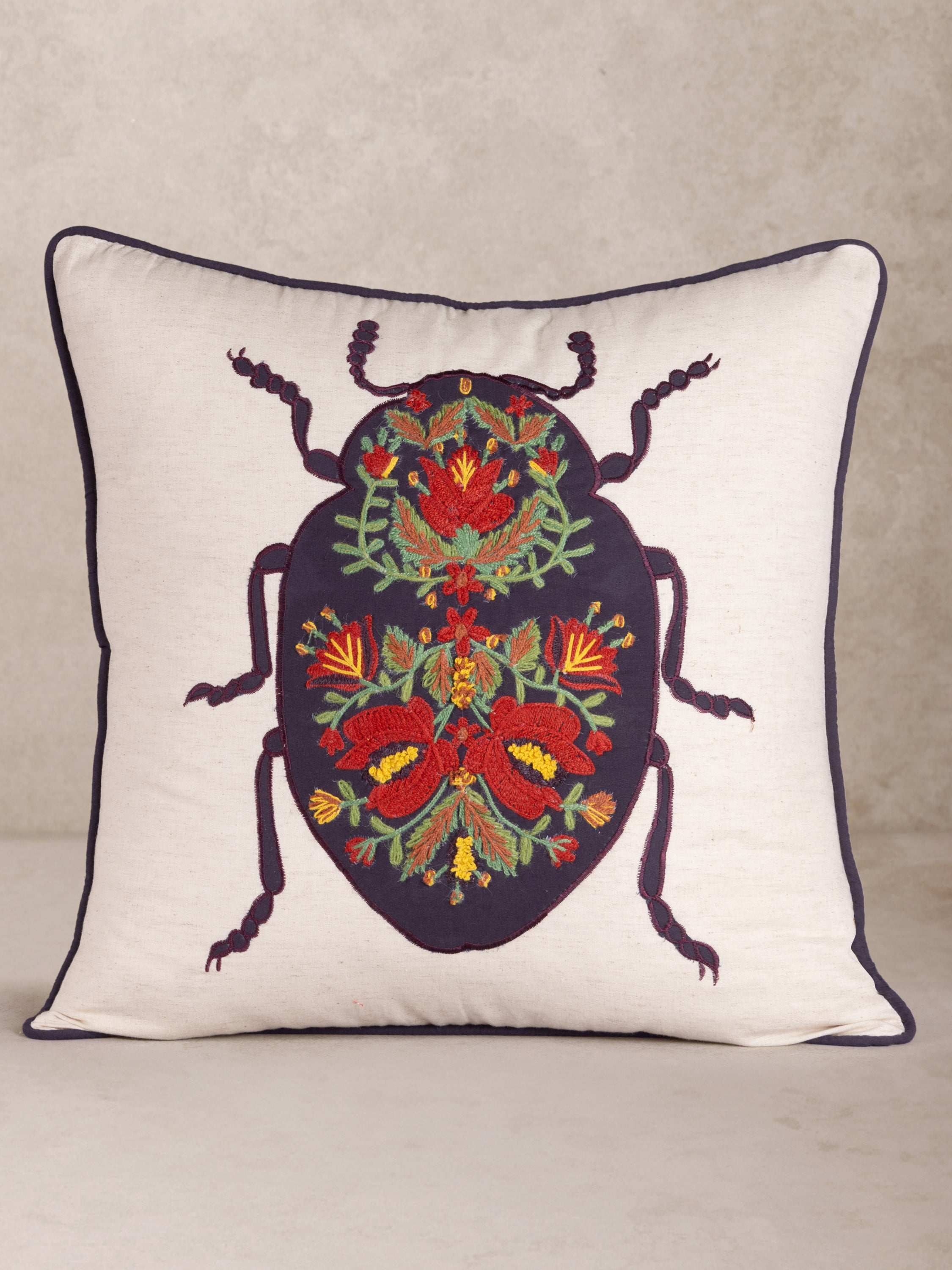 Handcrafted throw pillow in natural cotton with embroidered beetle and floral accents — artisan luxury accent
