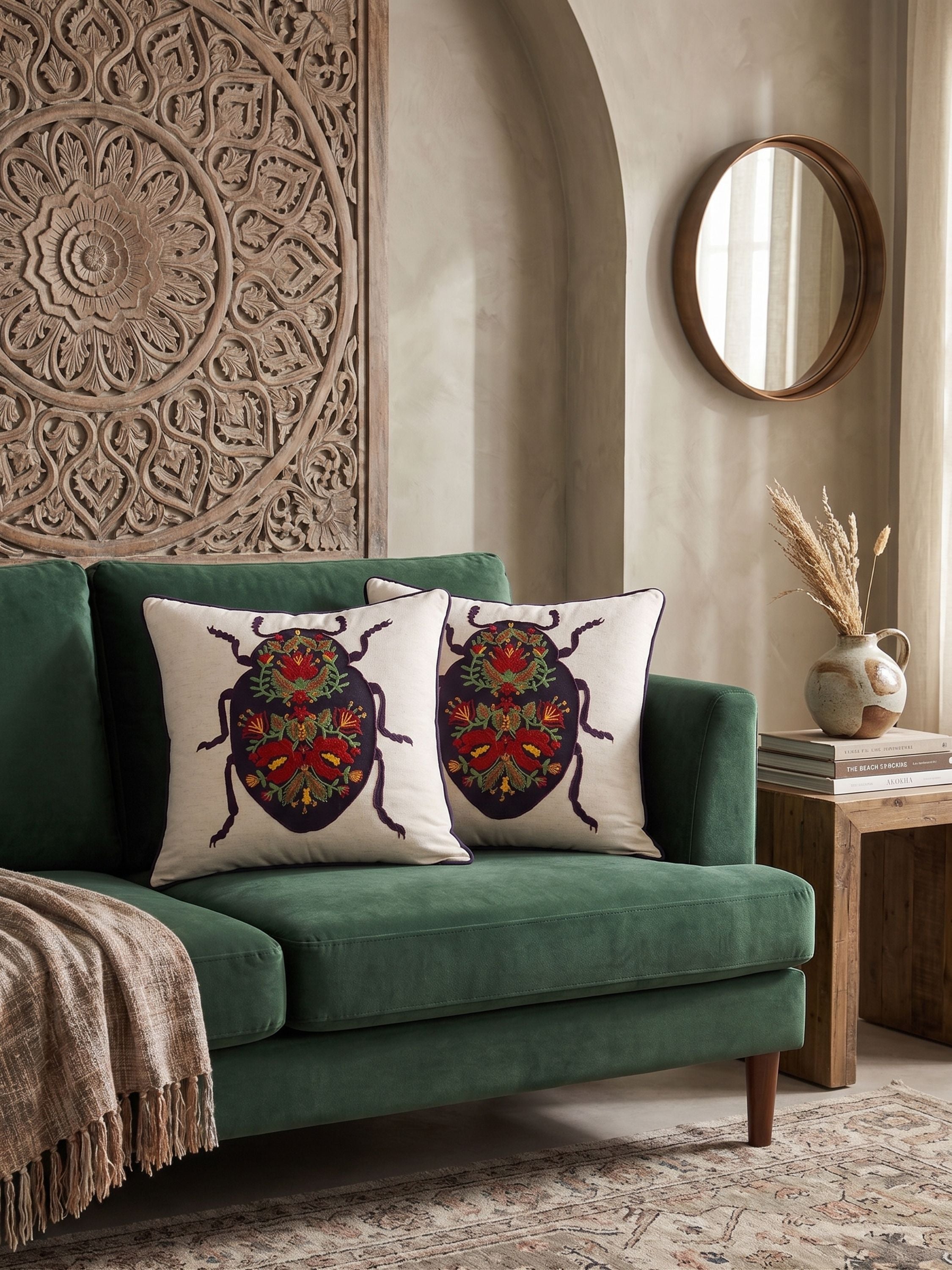 Hand embroidered beetle motif pillow cover in multicolor thread on ivory base styled on a green sofa with carved wood wall panel backdrop