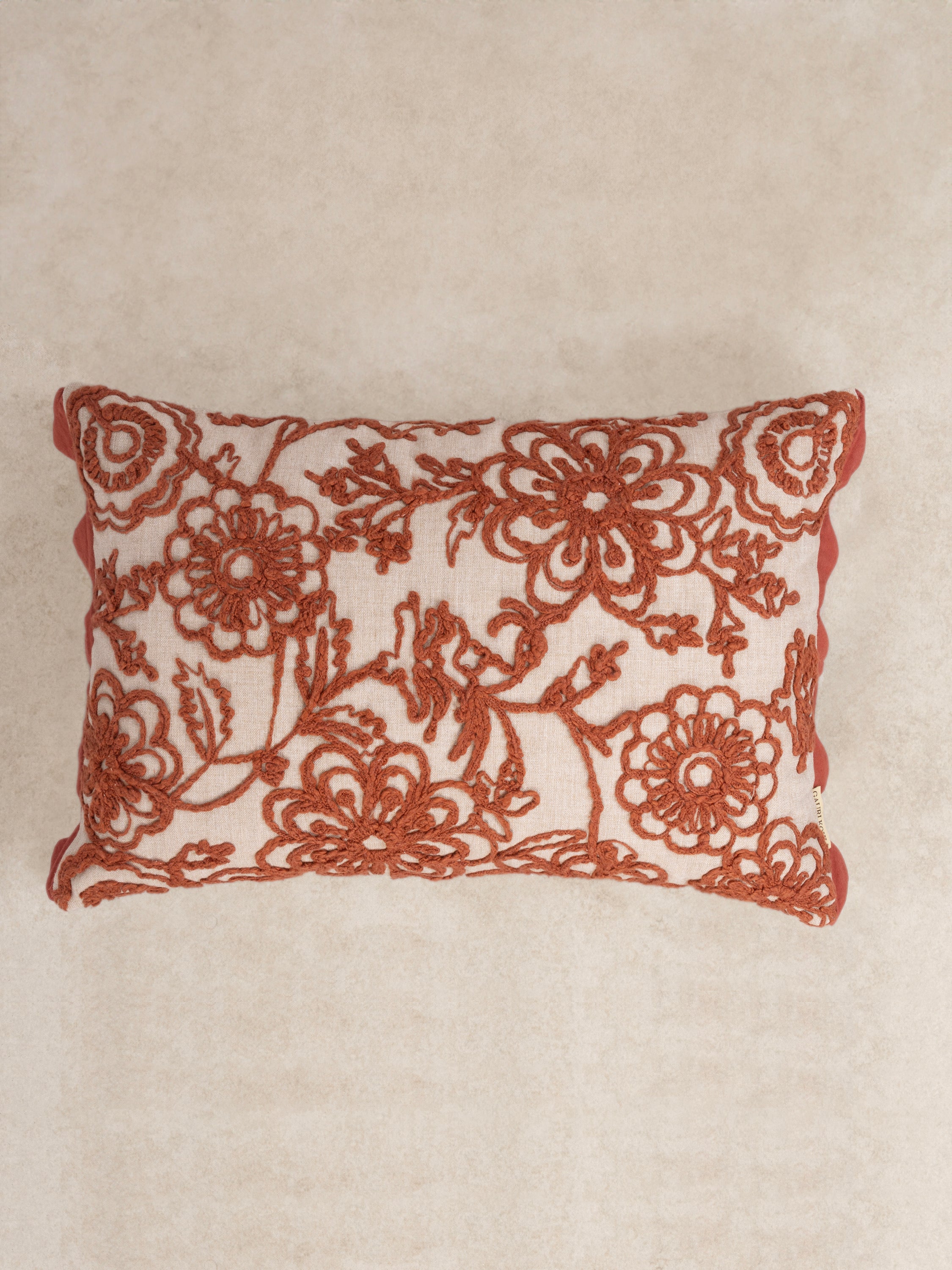 Handcrafted natural cotton pillow with embroidered floral motifs in warm rust tones — artisan luxury accent