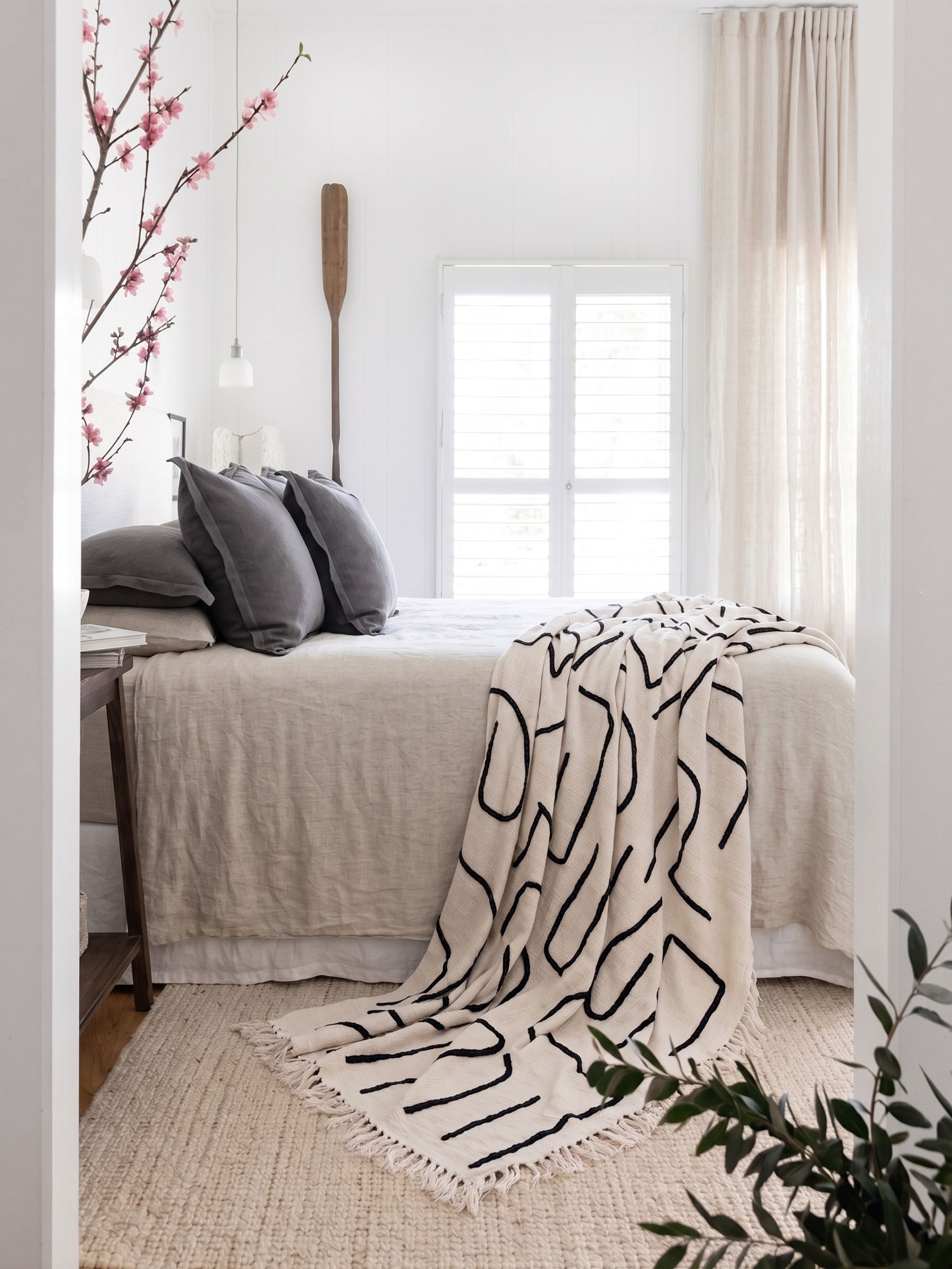 Slovenia ivory cotton throw blanket with an abstract black line pattern layered across a neutral bed in a minimal bedroom.