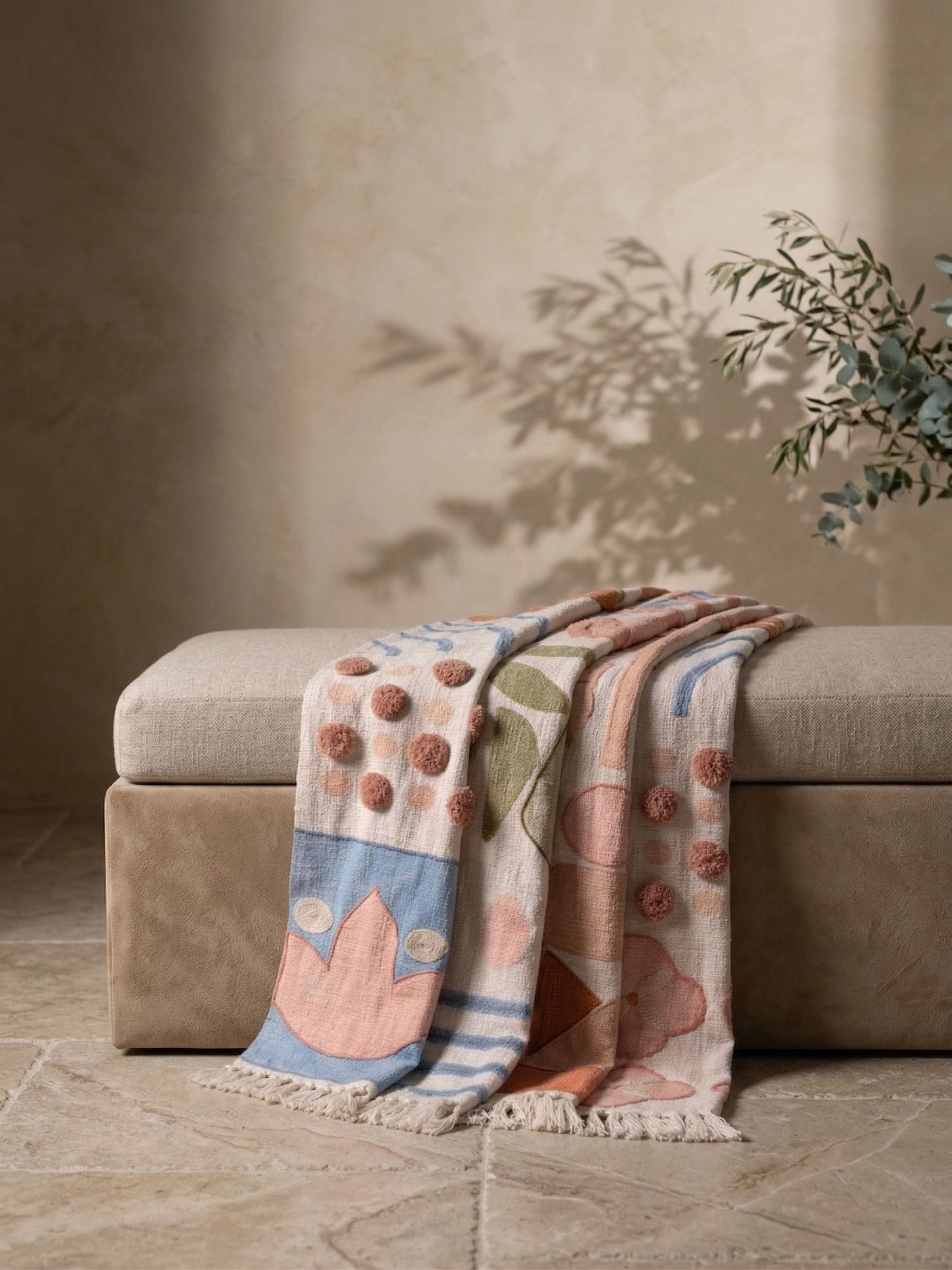 Hand embroidered cotton throw blanket with textured botanical and geometric motifs draped over a neutral upholstered bench
