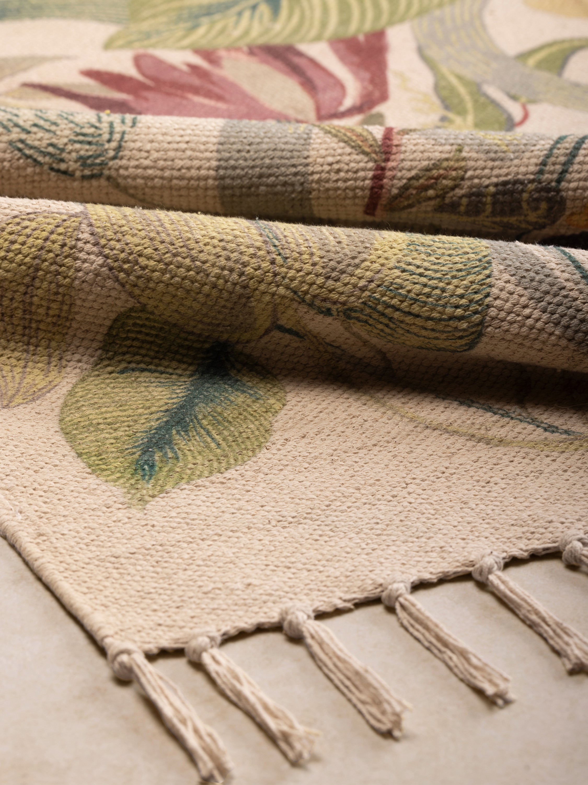 Close-up of rug showing printed botanical motifs, woven base, and fringe edge in neutral tones