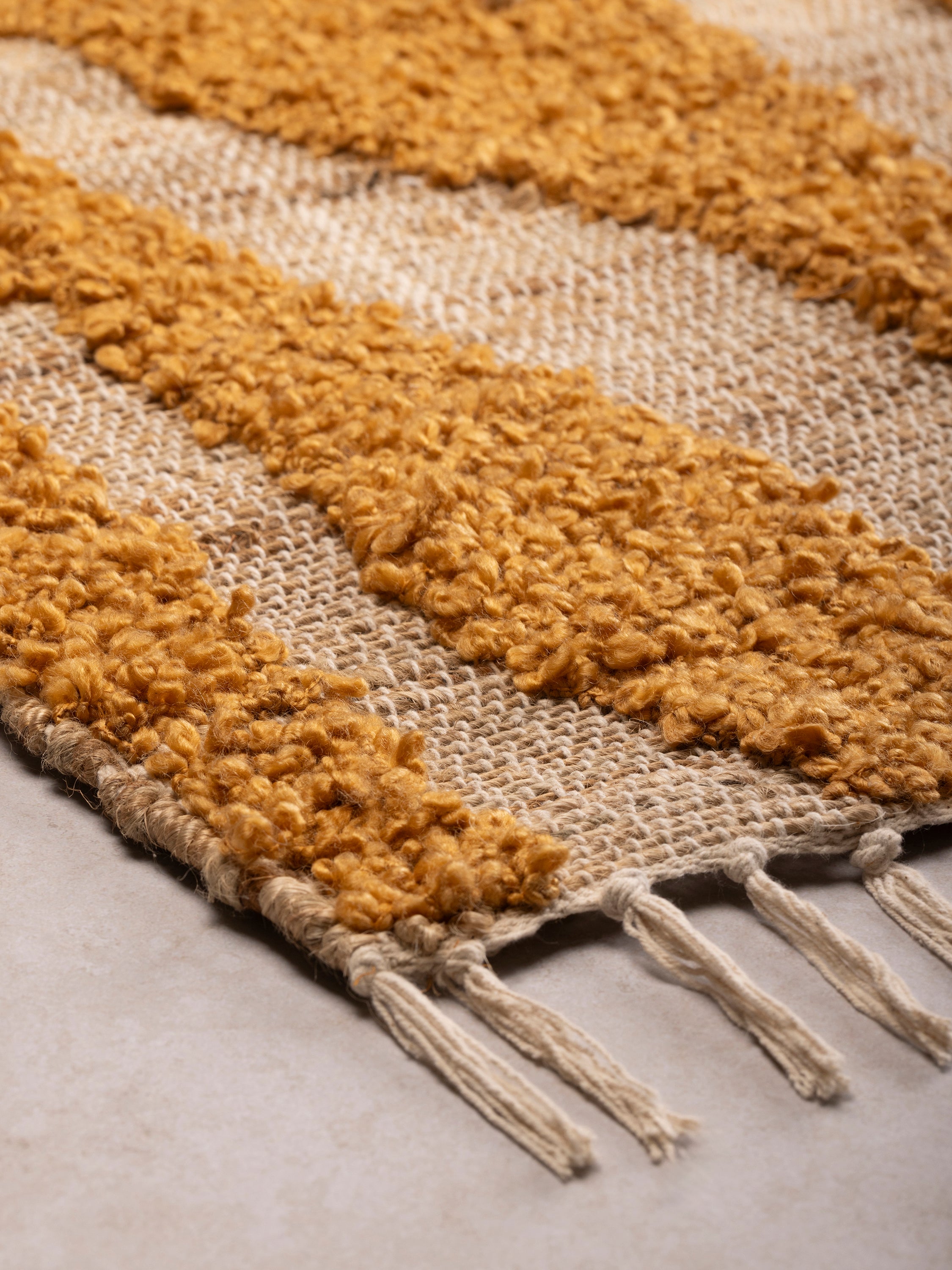 Close-up of rug corner showing thick pile texture, fringe edge, and alternating stripe pattern in warm tones
