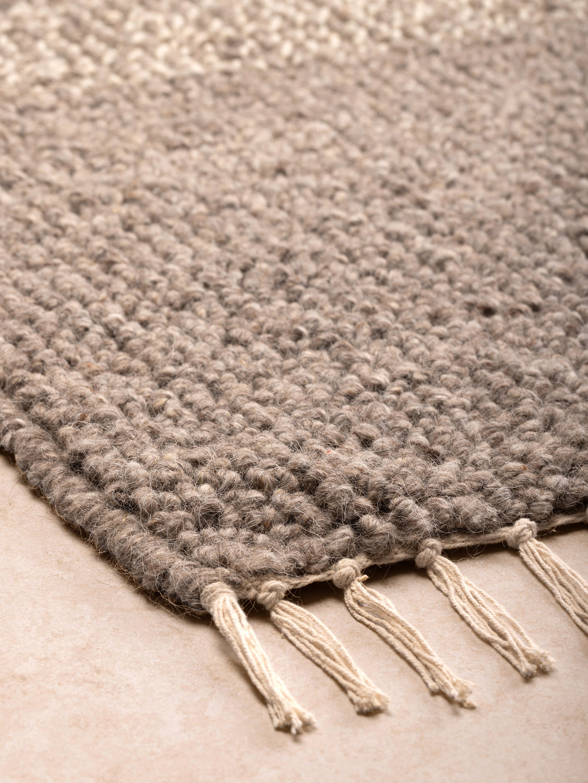 Wool and cotton rug corner detail showing chunky loop texture and twisted fringe edge.