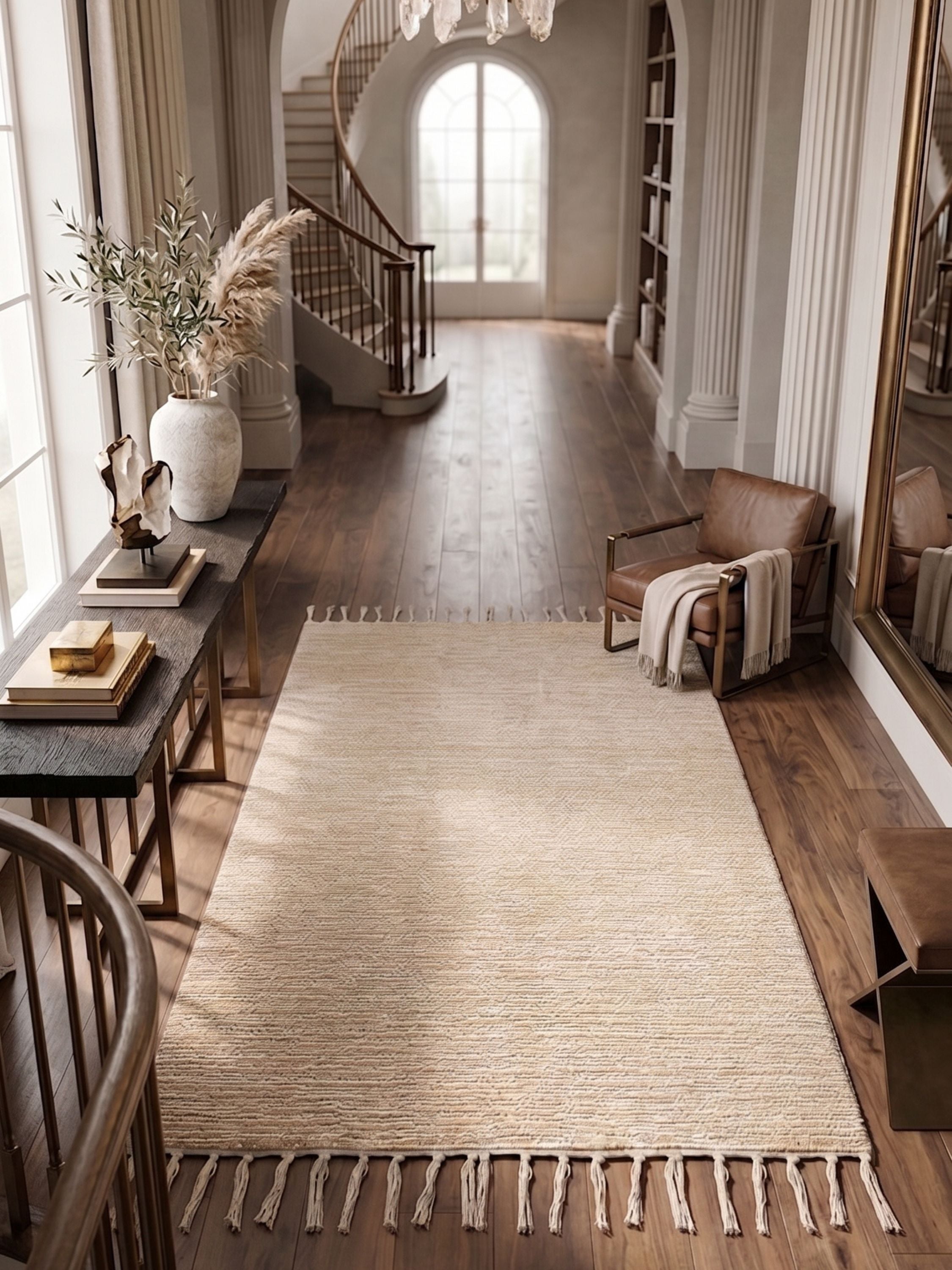 Handwoven neutral area rug with fringe detail styled in a refined entryway with dark wood flooring, sculptural decor, and soft natural light
