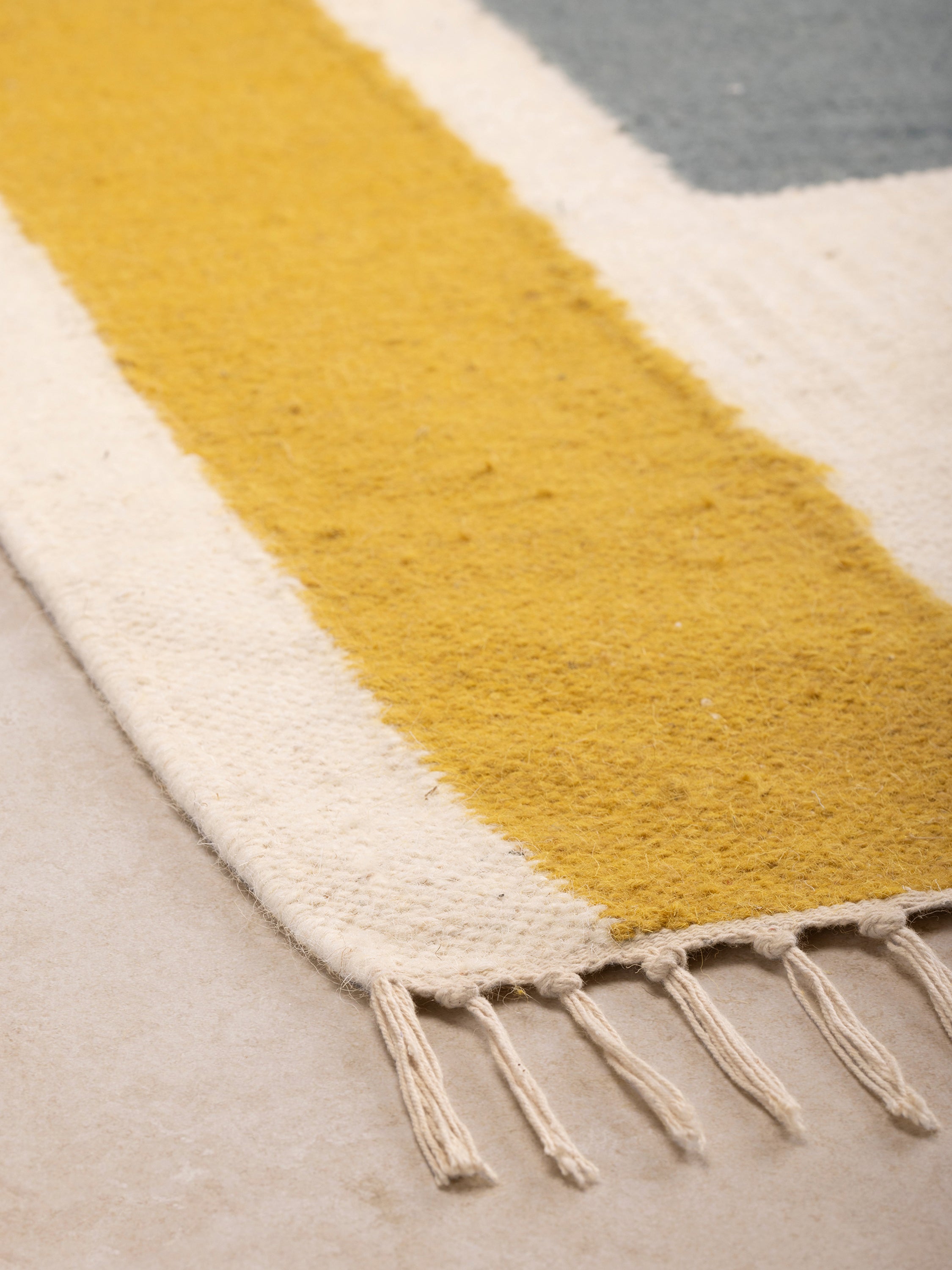 Close-up of the Horatio rug corner showing its woven texture, fringe edge, and color-block detailing in warm tones.