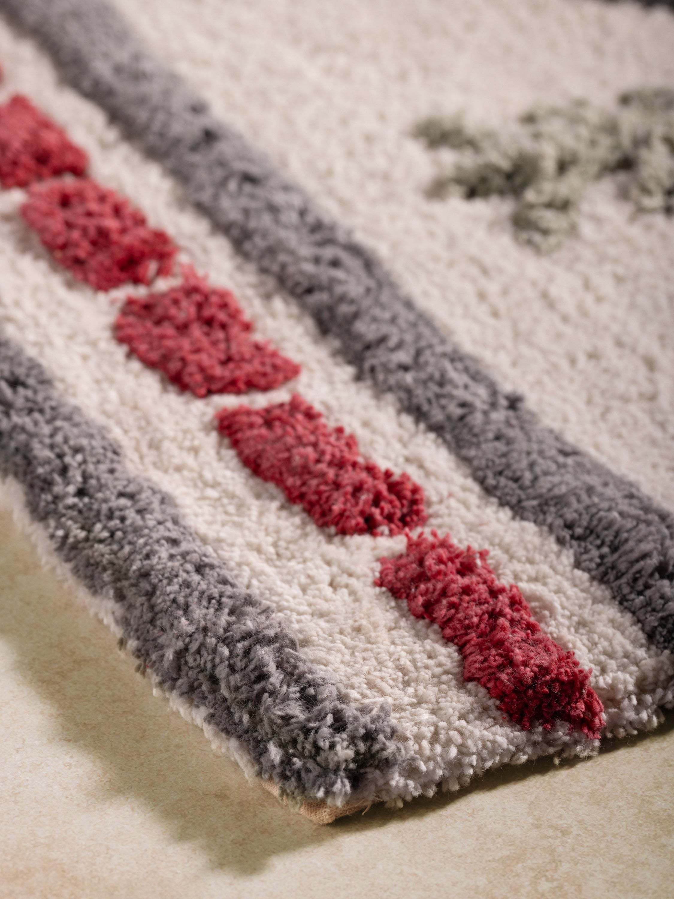 Close-up of the Gohana bath rug showing its raised border pattern in red tones and dense pile texture.