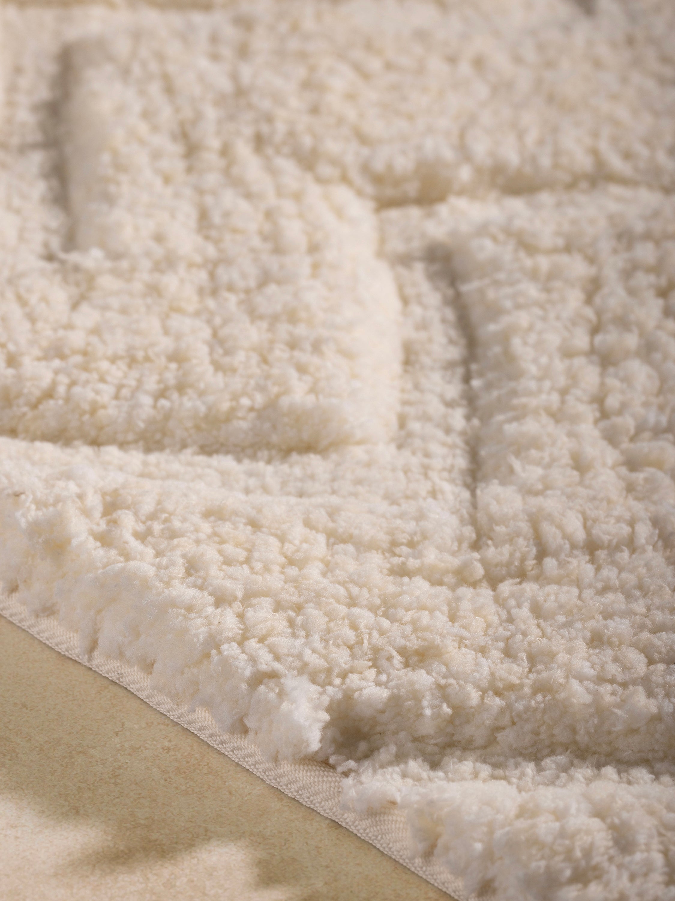 Close-up of ivory microfiber bath mat, raised chevron relief and dense pile texture.