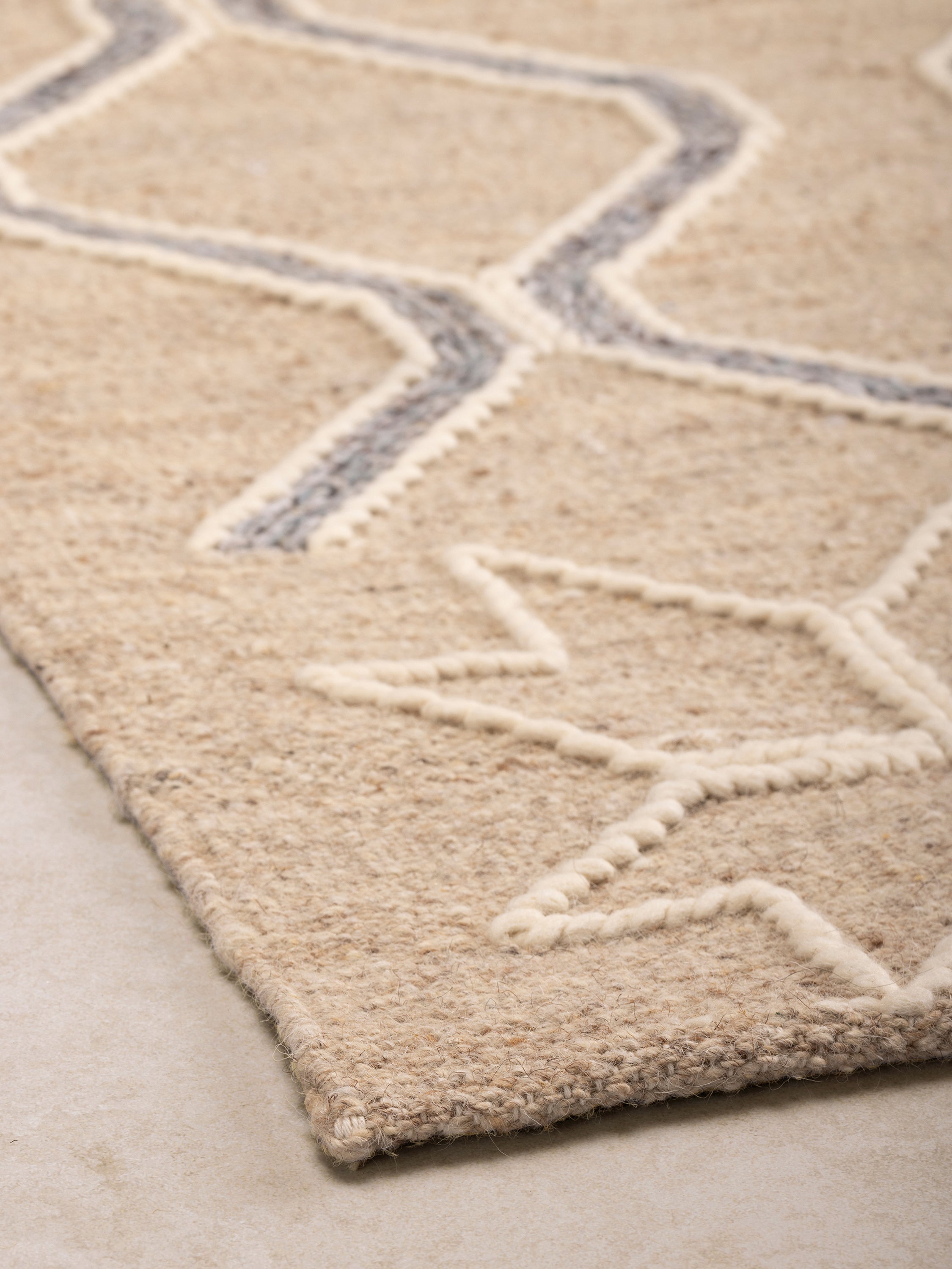 Close-up of rug corner showing raised geometric pattern and textured woven base with subtle tonal variation